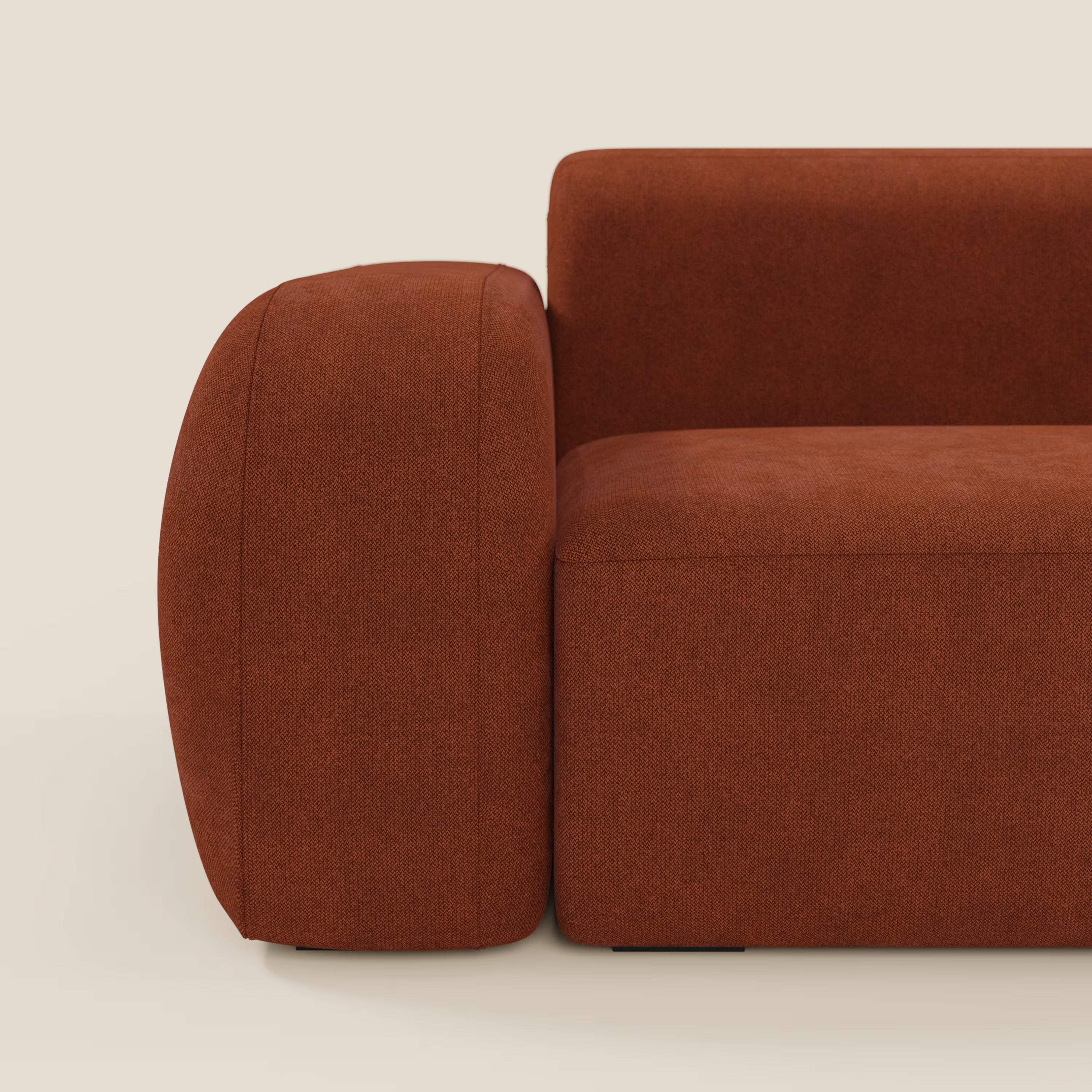 Un primo piano laterale del divano angolare componibile e modulare BonBon di Divani.Store, caratterizzato da un design squadrato in tessuto smacchiabile T23 ruggine con ampi braccioli e sedute in peluche su uno sfondo bianco sporco.