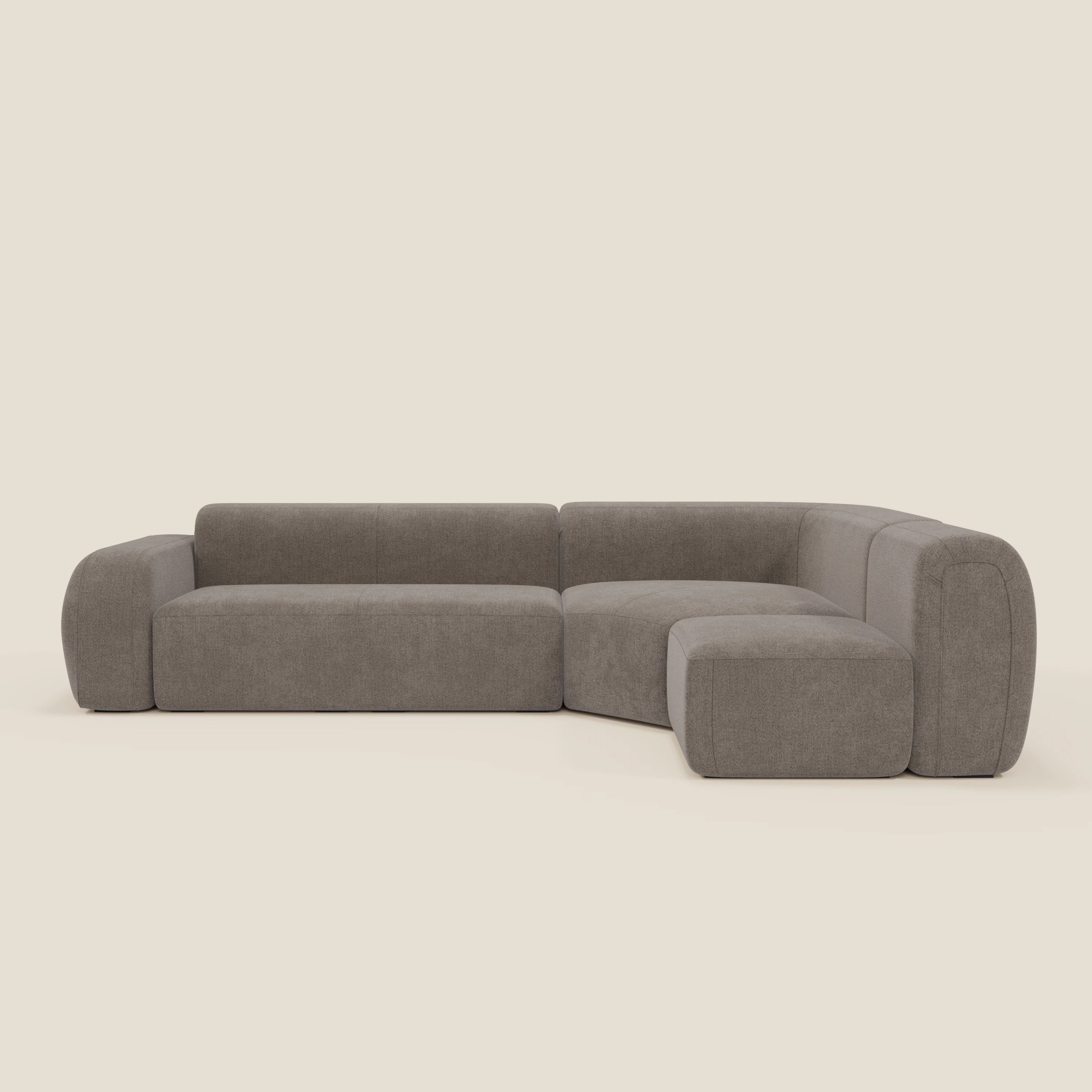 Il divano BonBon angolare componibile e modulare di Divani.Store in tessuto smacchiabile T23 talpa ha braccioli ampi e arrotondati, schienale basso e cuscini boxy per un look moderno su uno sfondo bianco sporco.