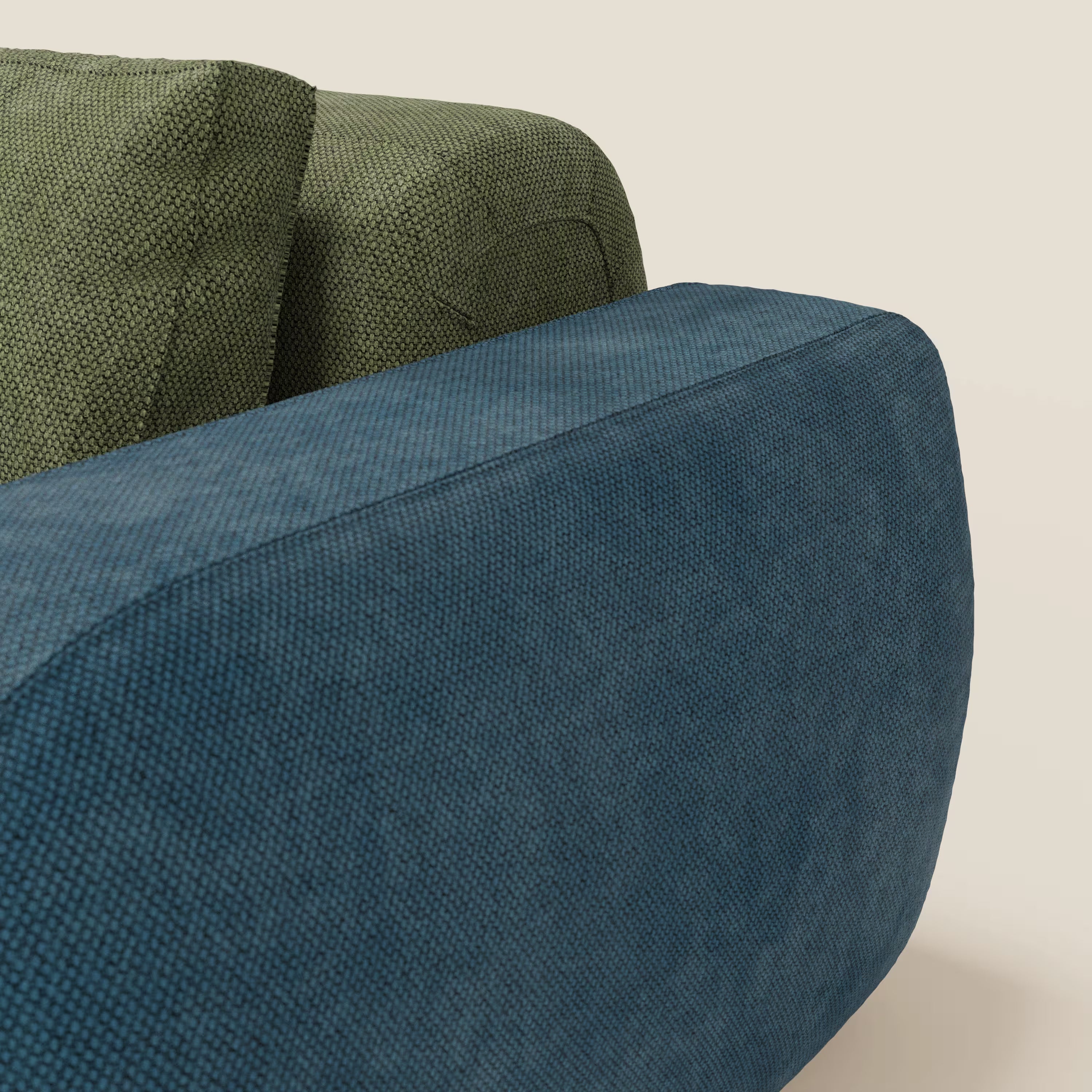 Primo piano del divano componibile BonBon 3 sedute - edizione Grande Fratello di Divani.Store, presentato in tessuto blu testurizzato con cuscino di schienale verde su uno sfondo beige, che evidenzia l'artigianalità italiana. È visibile solo una parte del divano.