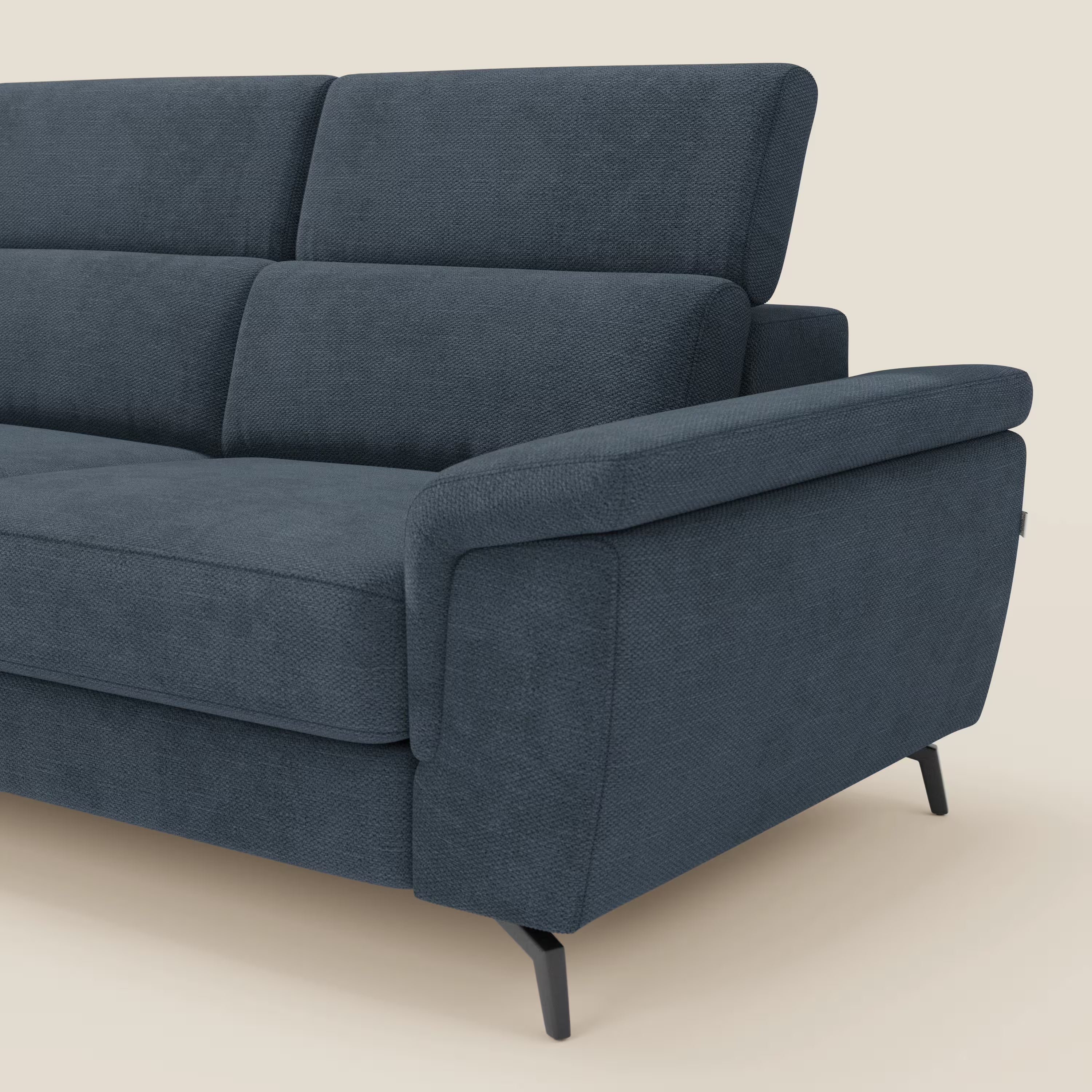 Primo piano del lato destro del divano angolare Estro di Divani.Store in tessuto impermeabile blu T14, con ampi braccioli imbottiti, schienali morbidi, gambe in metallo nero e poggiatesta regolabili, su uno sfondo beige chiaro.