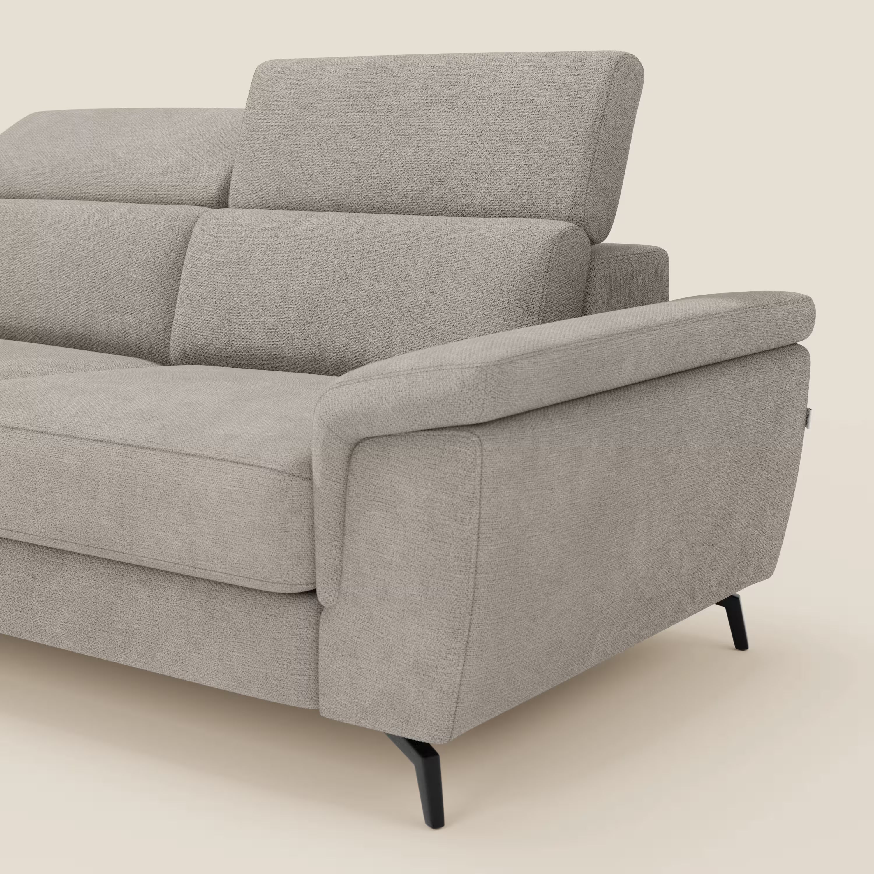 L'Estro Divano 3 posti con pouf estraibile di Divani.Store è caratterizzato da poggiatesta reclinabili, tessuto impermeabile T14 tortora, ampi braccioli e gambe nere sottili. L'immagine mostra un bracciolo e una seduta su sfondo beige.