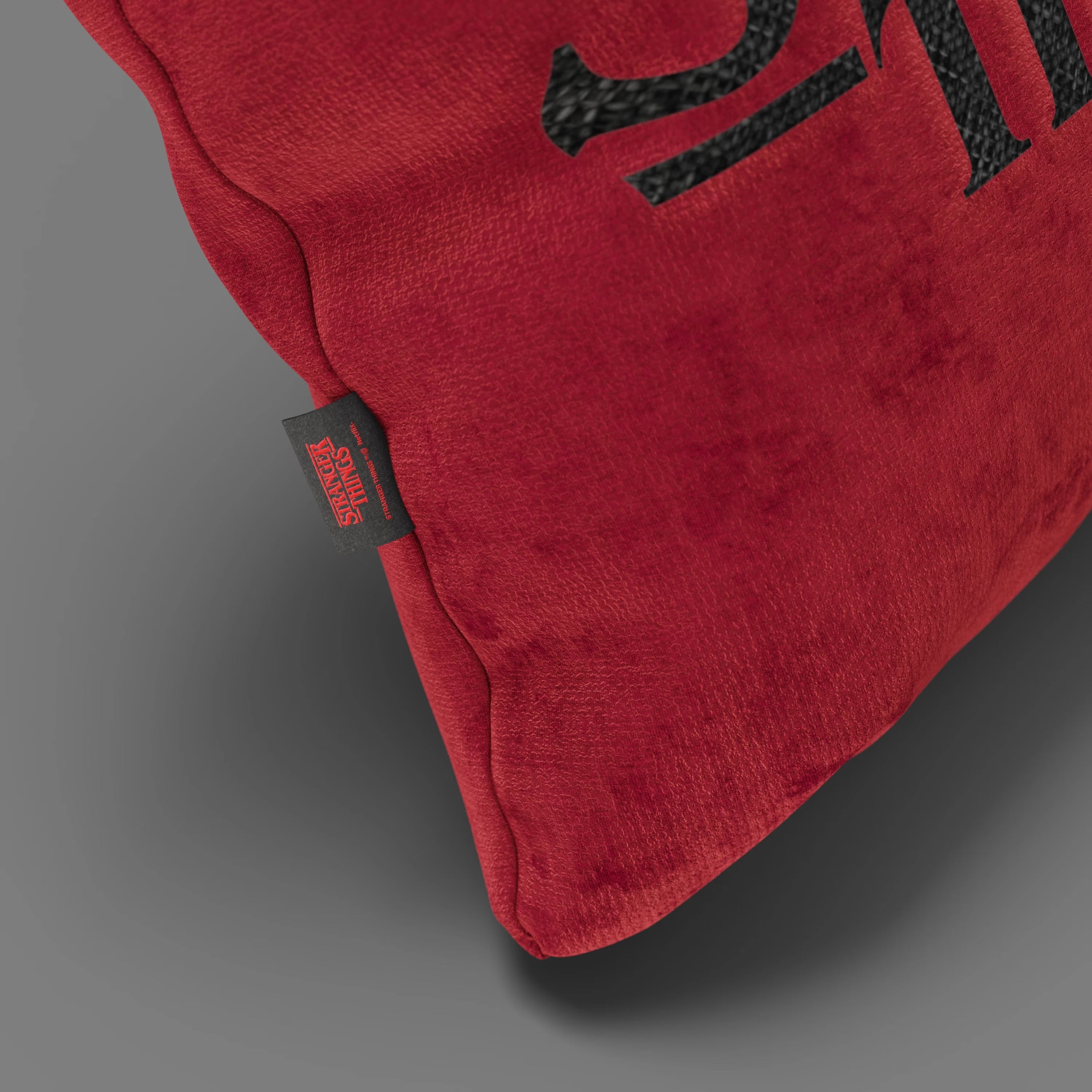 Primo piano del Cuscino Stranger Things Limited Edition con Ricamo di Divani.Store, un cuscino antimacchia rosso di 45x45 cm, con testo nero e targhetta "STRANGER THINGS 4", su sfondo grigio.