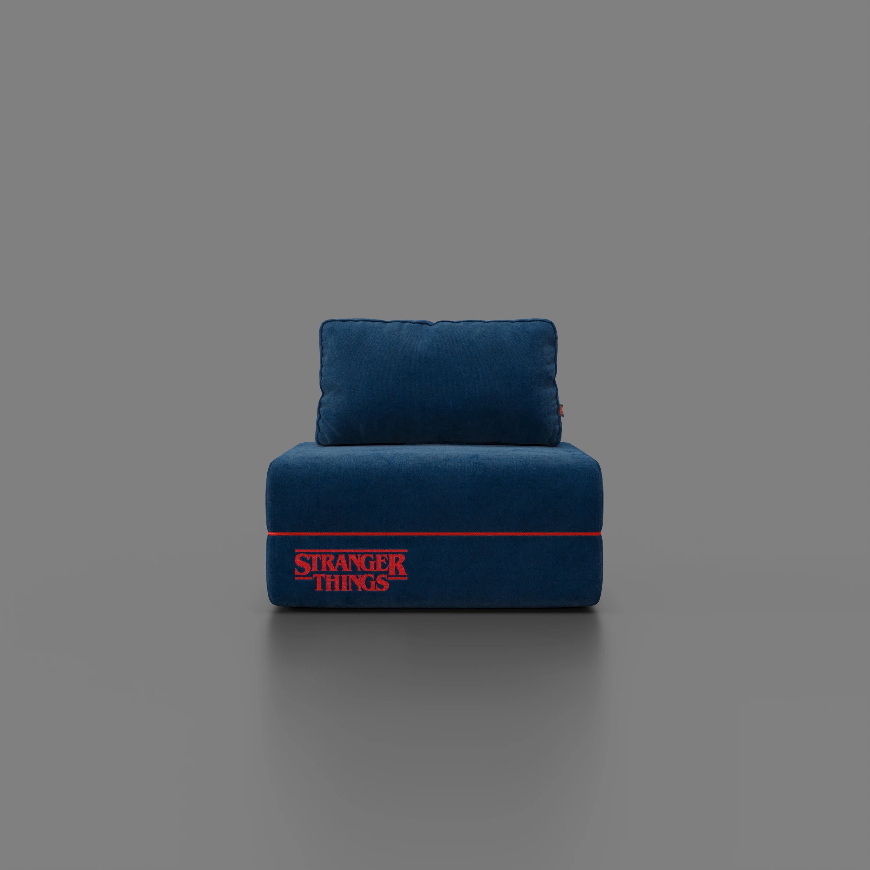 Una poltrona letto Rift blu STRANGER THINGS Edition di Divani.Store, con materasso in memory foam alto 22 cm e tessuto antimacchia, è posizionata al centro di uno sfondo grigio. Il logo rosso di Stranger Things, con una linea sottile, compare sulla parte anteriore.