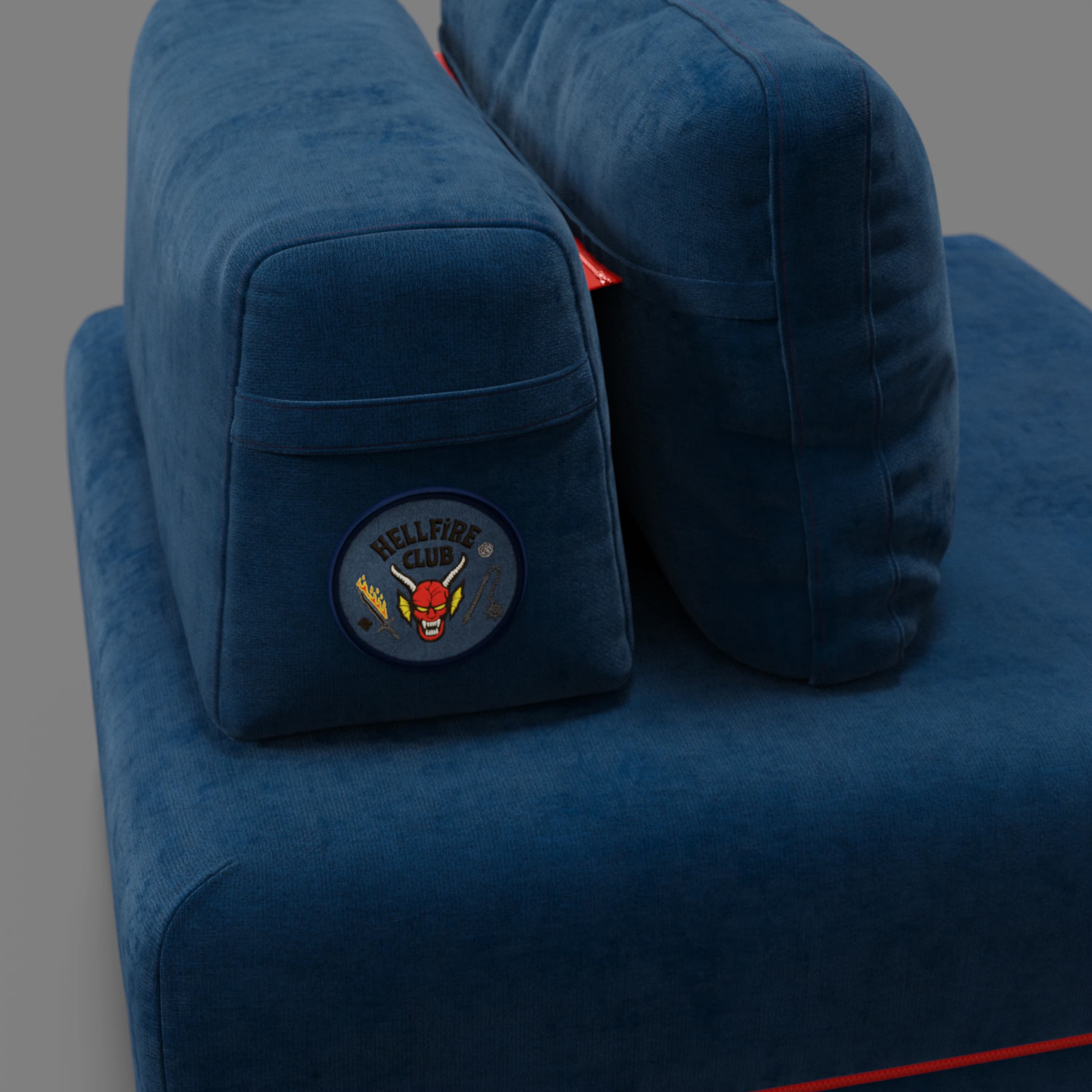 Primo piano della poltrona letto Divani.Store Rift STRANGER THINGS Edition in tessuto blu antimacchia, con materasso in memory foam da 22 cm e cuscino con patch "Hellfire Club". L'ambientazione è a tinta unita grigia e blu.