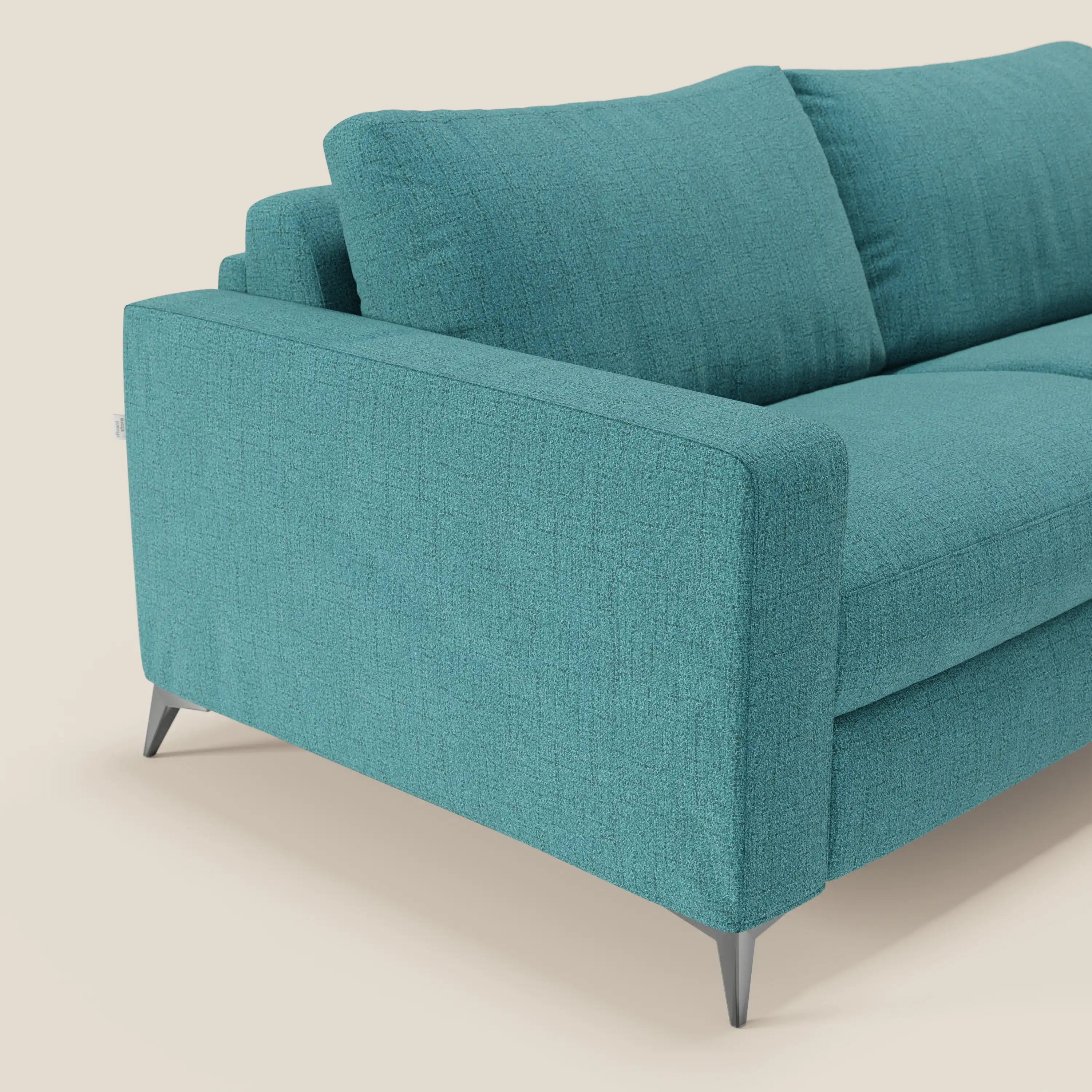 Il letto matrimoniale Alaya Divano di Divani.Store, in tessuto impermeabile T03 azzurro, è caratterizzato da cuscini morbidi, linee pulite, gambe metalliche angolate e cuscini di schienale in feltro per un design minimalista su uno sfondo beige neutro. Focus: braccio sinistro e cuscini.