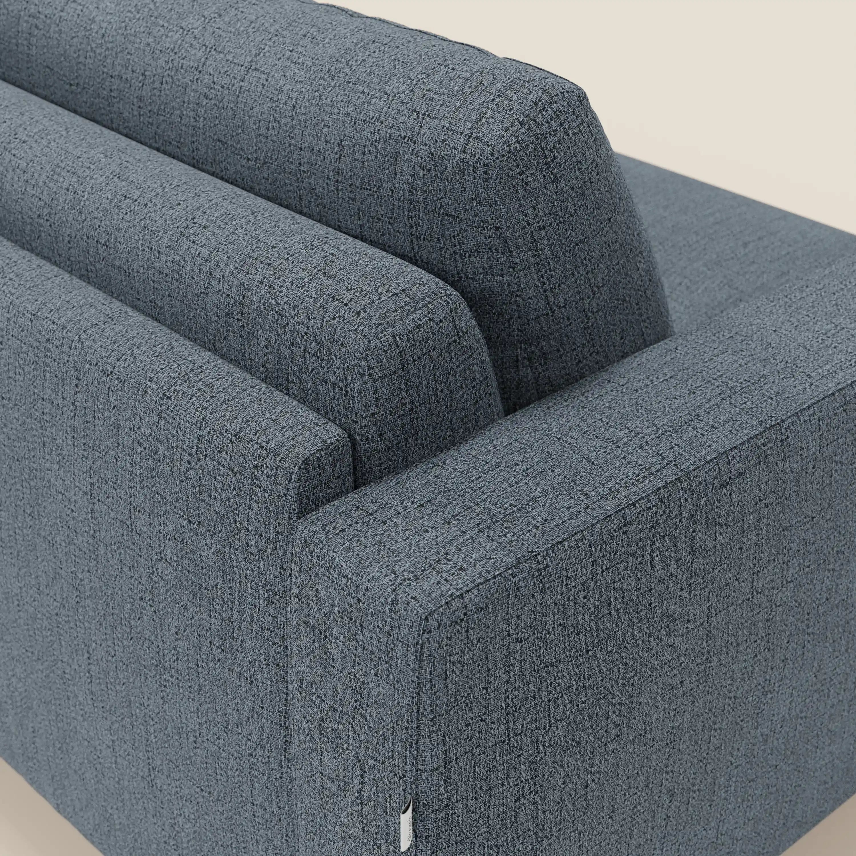 Una vista ravvicinata e angolata del letto matrimoniale Alaya Divano di Divani.Store in tessuto impermeabile T03 blu, che evidenzia il suo stile minimale con linee pulite, schienale, bracciolo e una piccola targhetta bianca. Lo sfondo è beige chiaro.