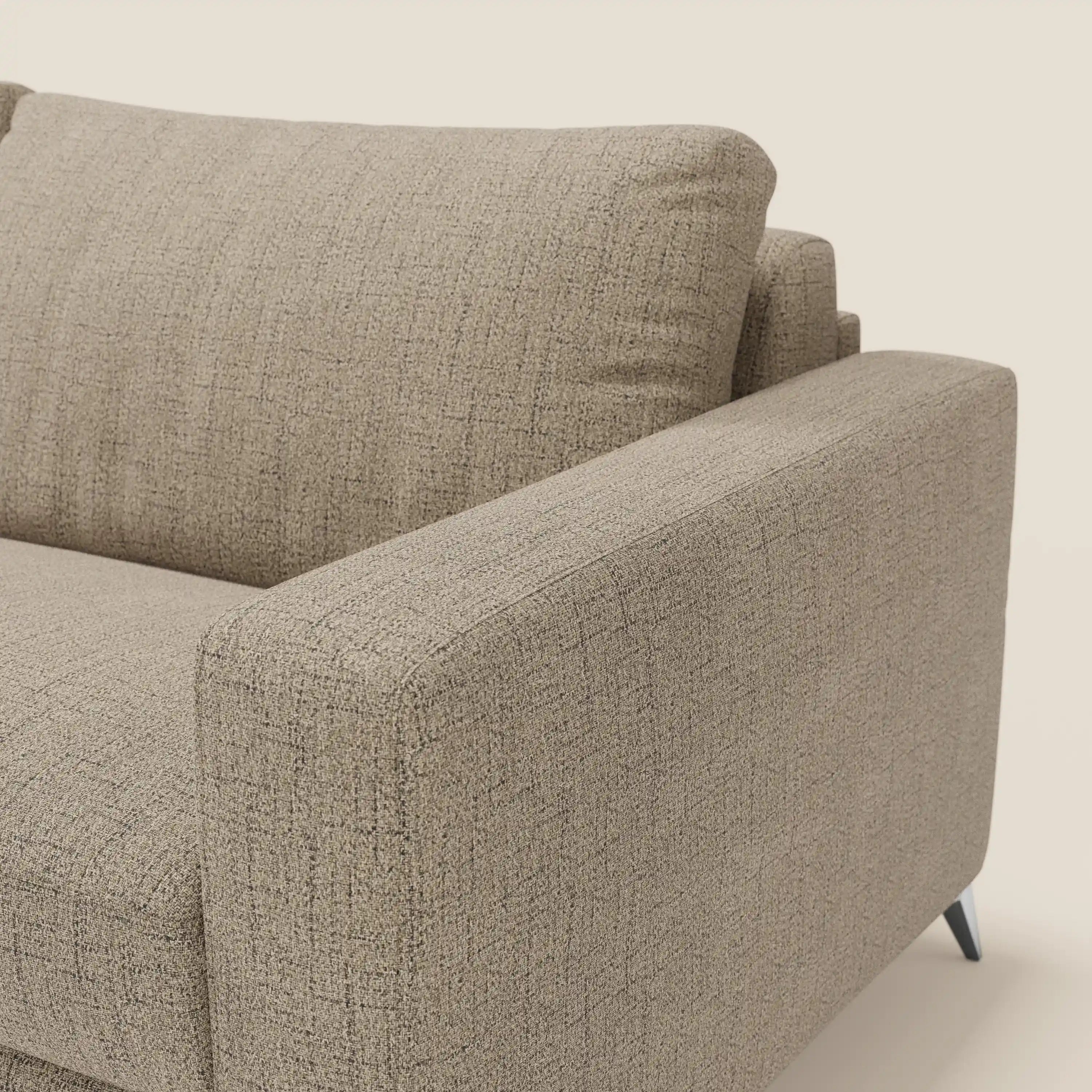 Un primo piano del letto matrimoniale Alaya Divano di Divani.Store in tessuto impermeabile T03 marrone mostra un bracciolo, i morbidi e spessi cuscini della seduta e dello schienale, l'imbottitura in trama e le sottili gambe in metallo scuro su uno sfondo beige.