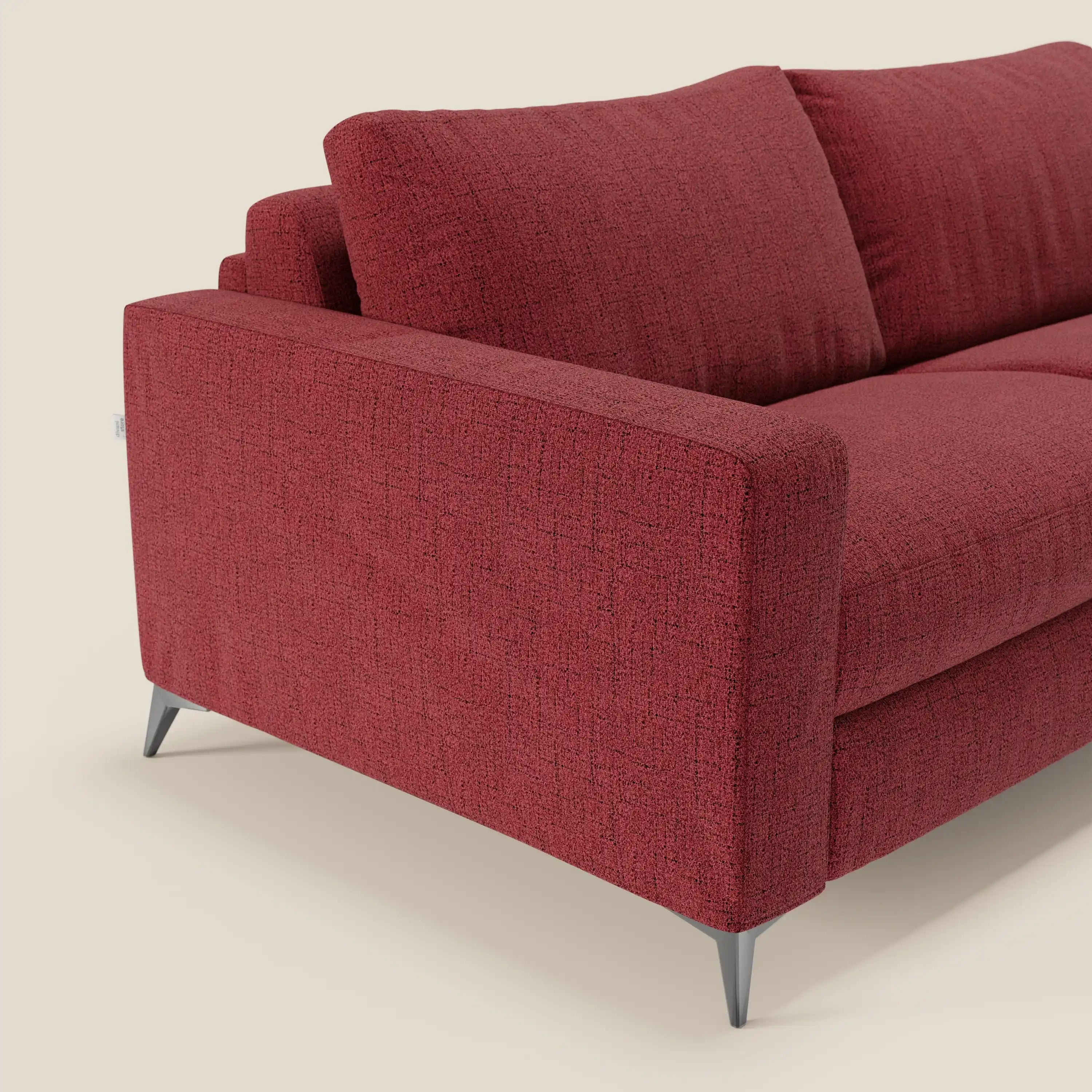 Un primo piano del letto matrimoniale Alaya Divano di Divani.Store in impermeabile T03 rosso ne mostra la texture, il bracciolo angolato, i cuscini in feltro e le eleganti gambe in metallo, sottolineando il suo design minimale su uno sfondo bianco sporco.