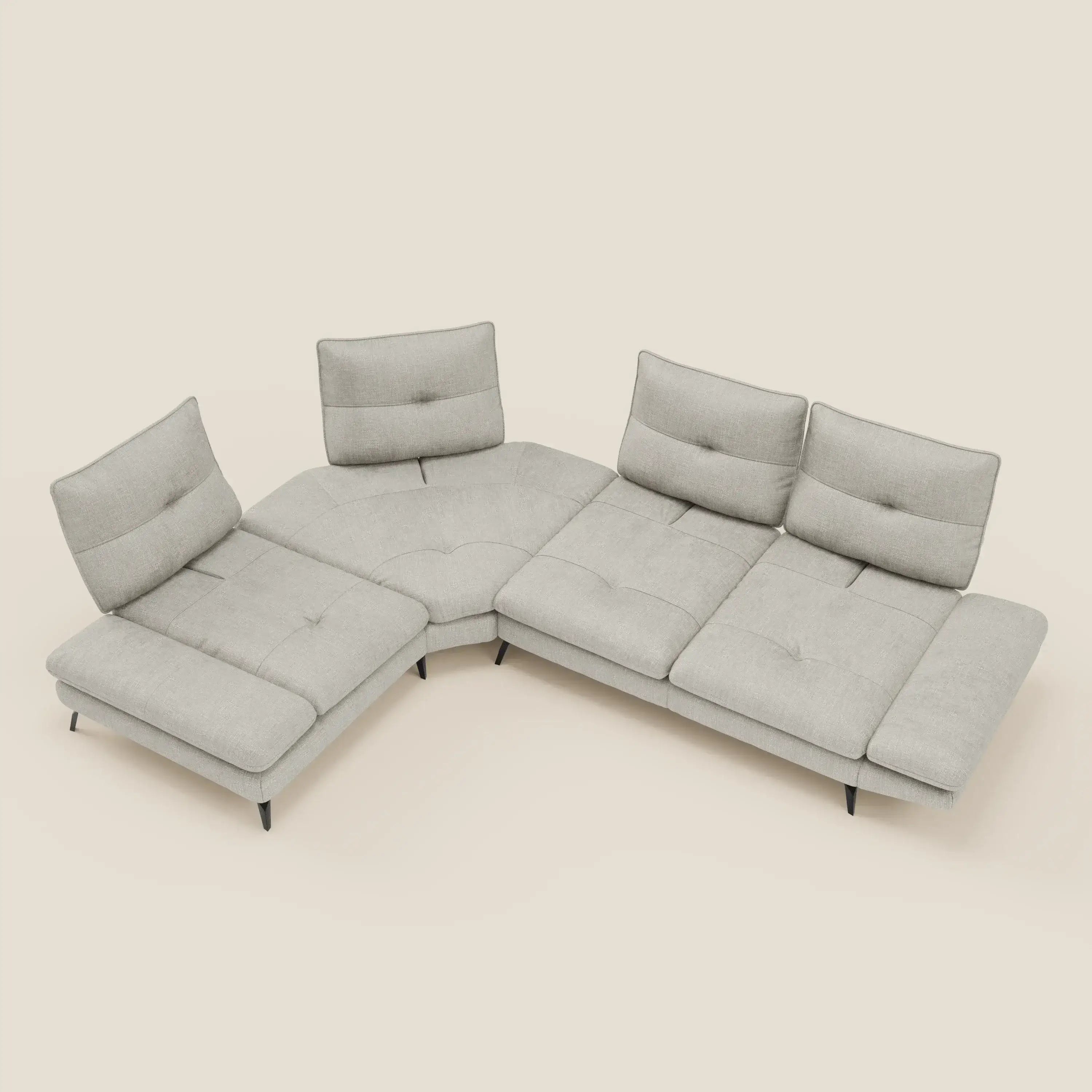 Ardex Divano Angolare di Divani.Store è caratterizzato da quattro sedute, schienali traslanti, bracciolo regolabile ed elegante rivestimento in tessuto impermeabile T06 grigio chiaro. Poggiato su basse gambe nere e cuscini trapuntati, si staglia su uno sfondo bianco sporco.