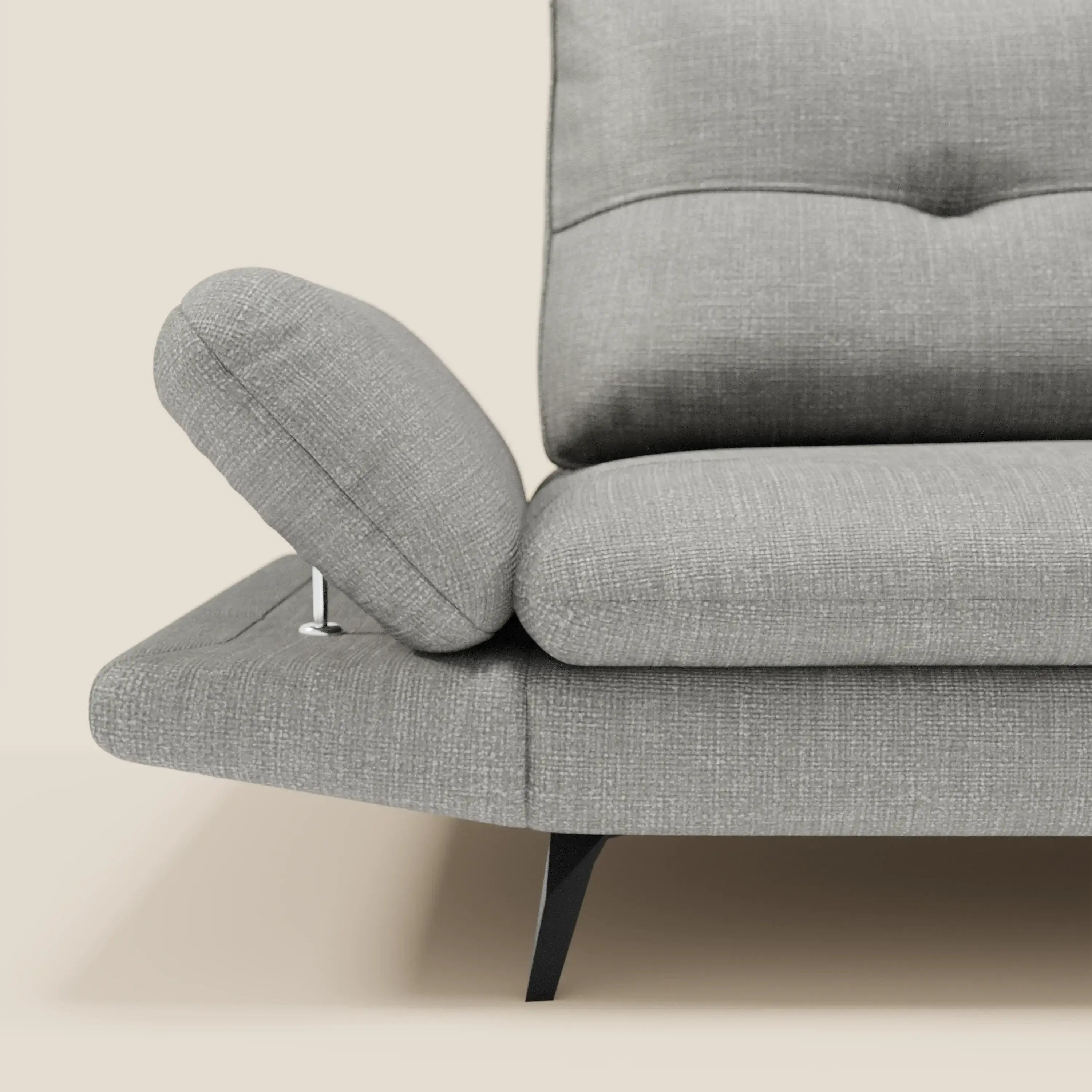 Un primo piano di Ardex Divano 3 posti di Divani.Store in impermeabile T06 grigio mostra un bracciolo regolabile in rilievo su una cerniera in metallo, con schienali traslanti, dettagli in tufting, linee angolari e gambe affusolate nere su uno sfondo beige.