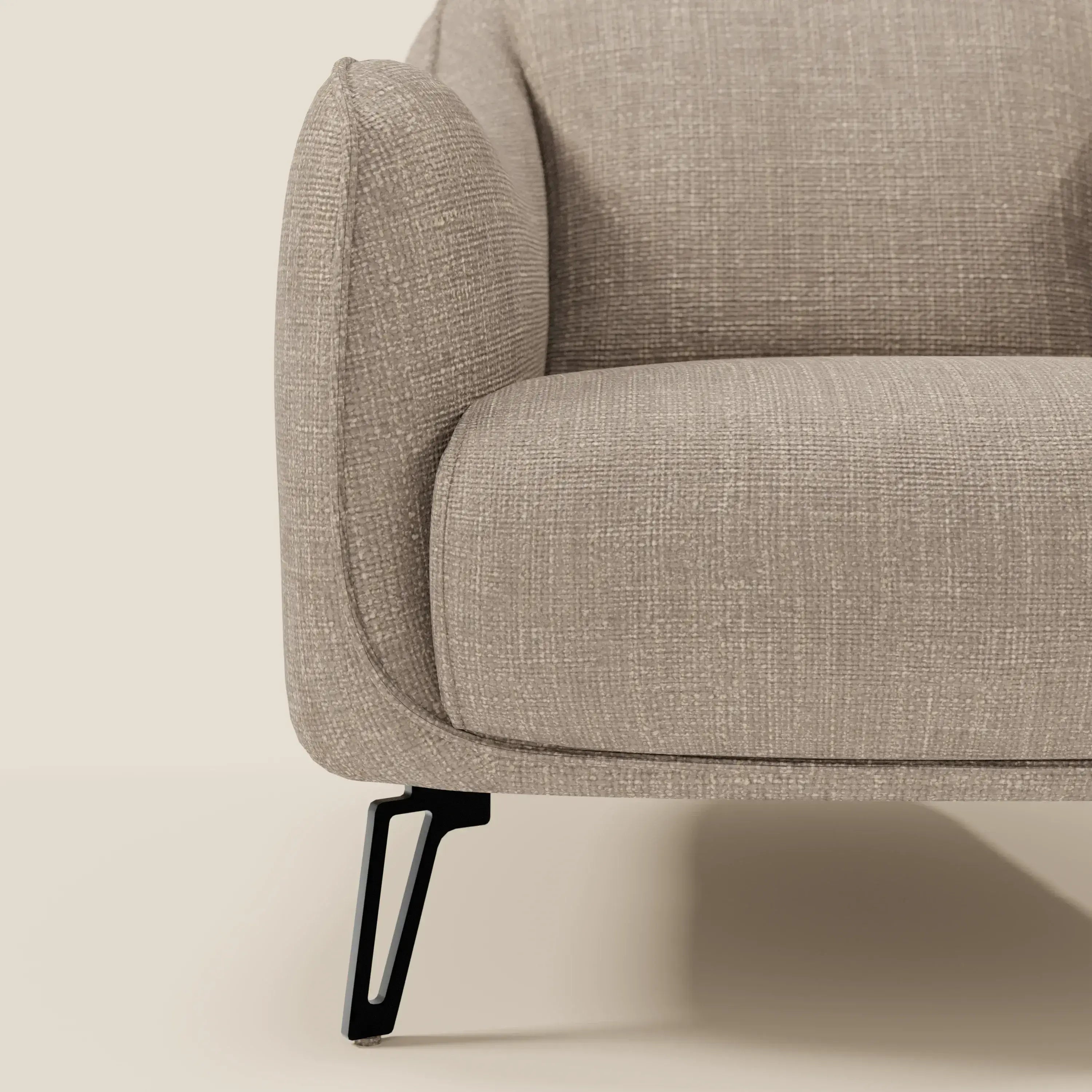Primo piano di Avela Poltroncina di Divani.Store in morbido tessuto impermeabile T06 tortora, con bracciolo arrotondato, seduta imbottita e sottili gambe in metallo nero su sfondo neutro.