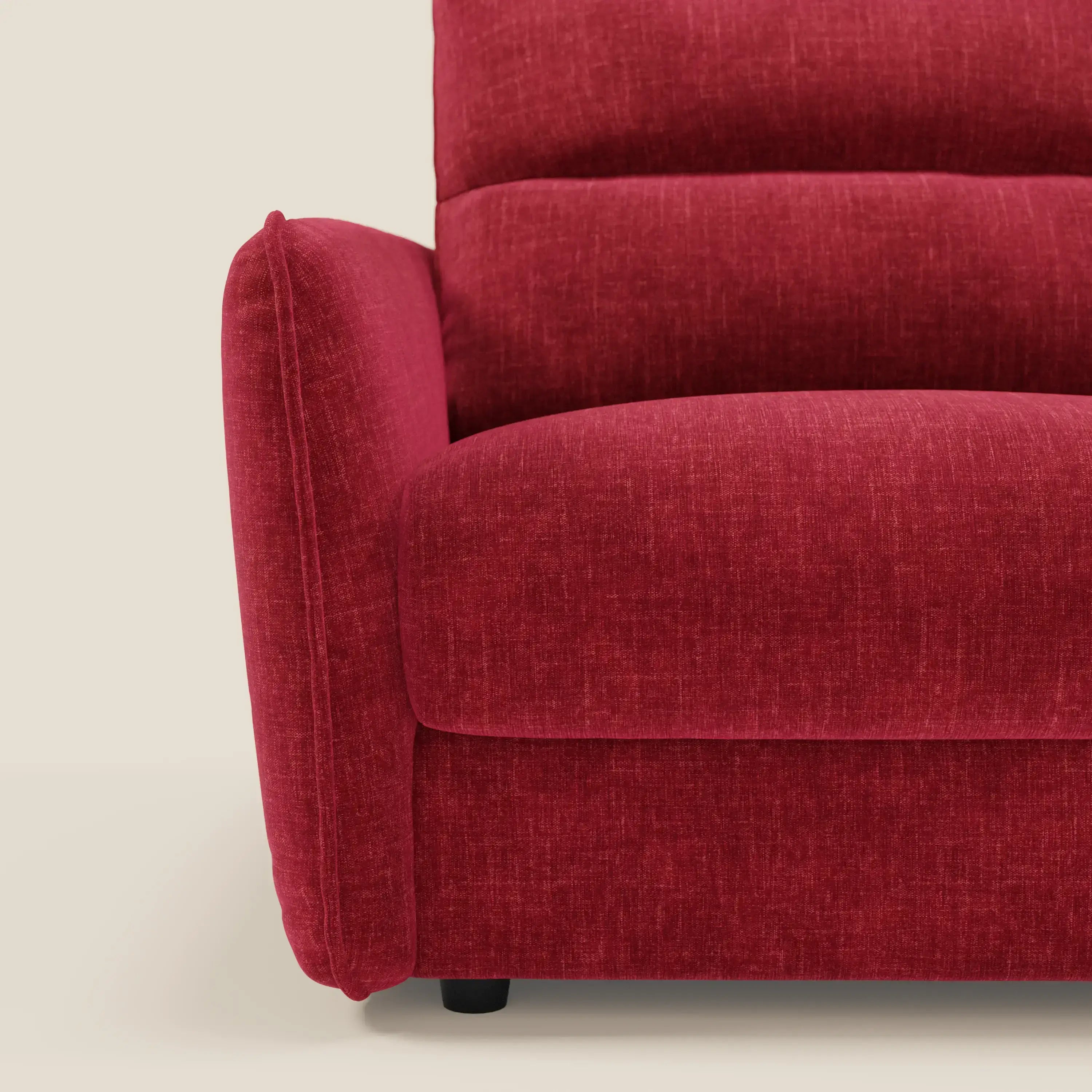 Primo piano del Divano letto Elios di Divani.Store in tessuto smacchiabile T24 rosso bordeaux, che mostra il bracciolo sinistro, lo schienale con morbidi cuscini, il cuscino di seduta e una gamba nera su uno sfondo bianco sporco.