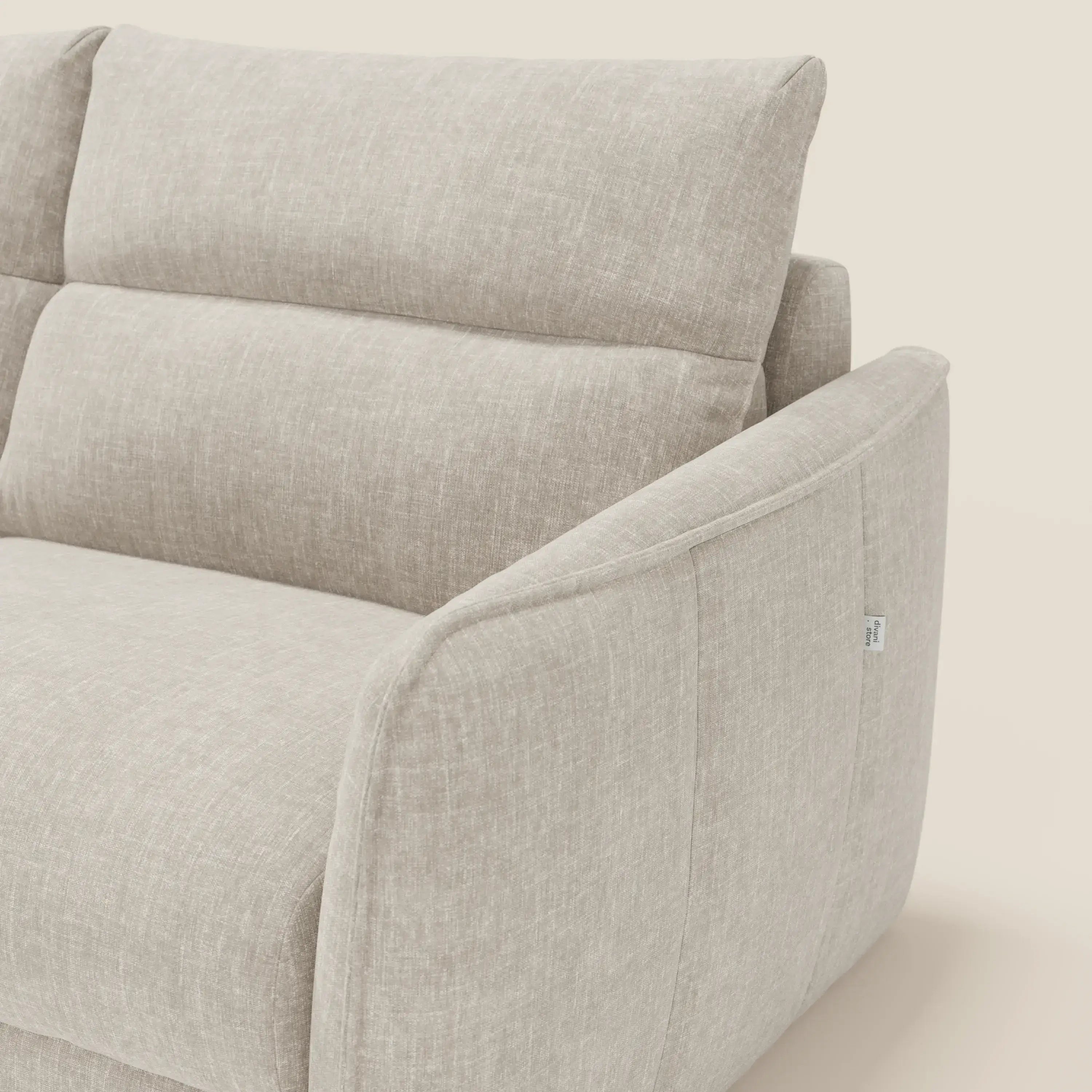 Un primo piano del divano letto Elios di Divani.Store in tessuto smacchiabile T24 bianco latte mostra i braccioli angolati e imbottiti, i cuscini dello schienale con cuciture orizzontali, il rivestimento in morbida texture e una piccola etichetta in tessuto sul braccio.