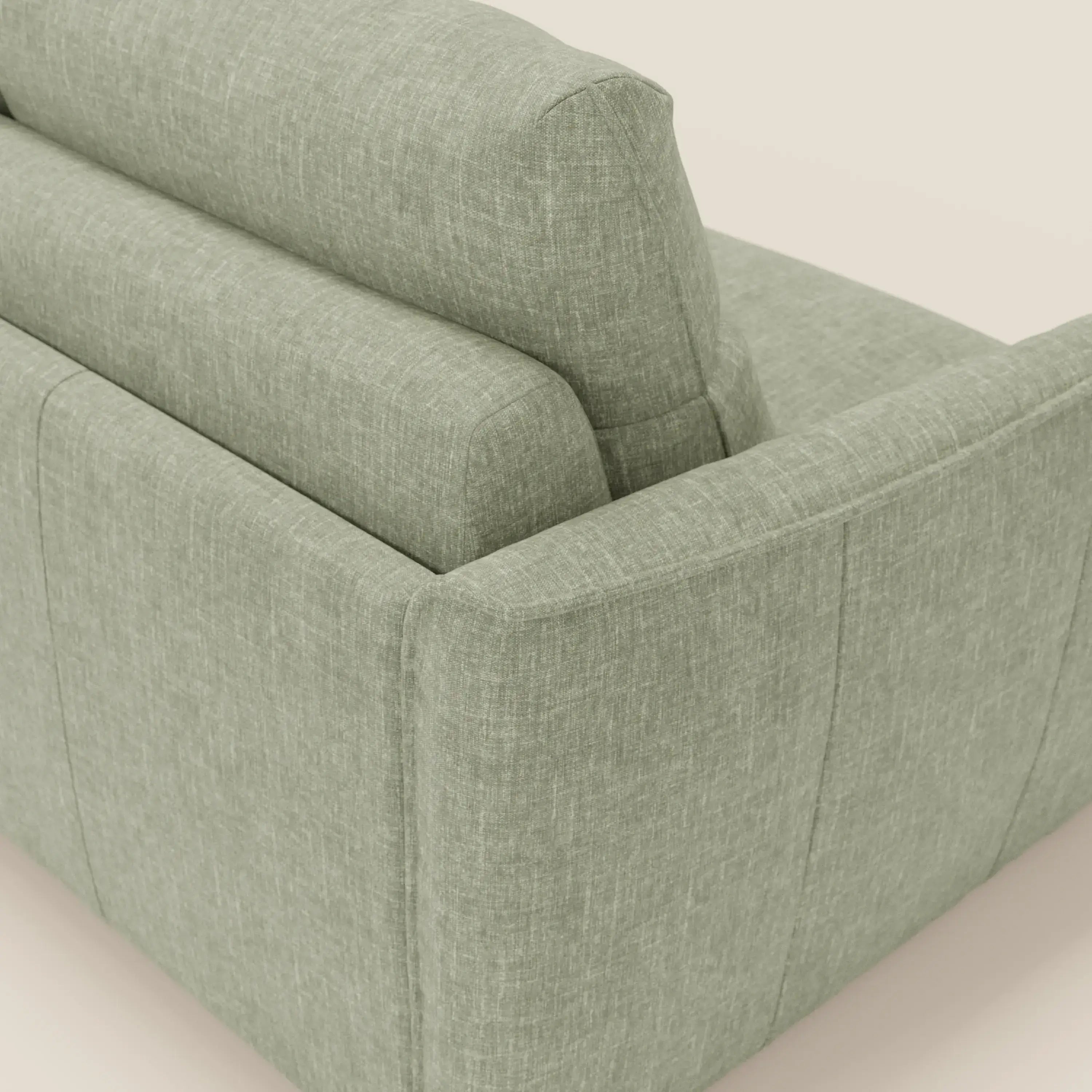 Un primo piano mostra lo schienale e il bracciolo di Elios Divano letto con morbidi cuscini spalliera in tessuto smacchiabile T24 verde salvia di Divani.Store, evidenziandone l'aspetto intrecciato e il design moderno su uno sfondo neutro.