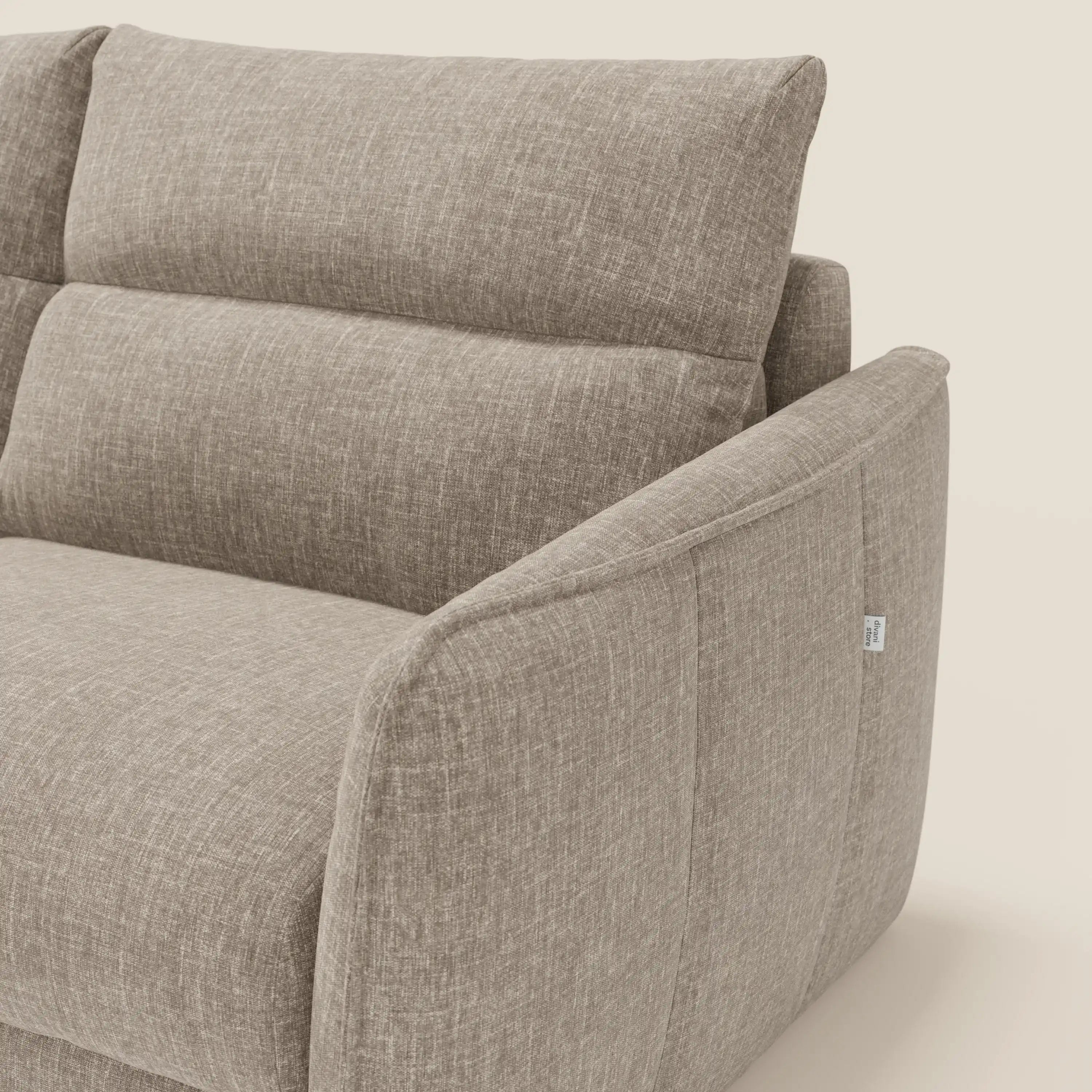 Un primo piano di Elios Divano letto con morbidi cuscini spalliera in tessuto smacchiabile T24 marrone tortora di Divani.Store ne evidenzia i bordi morbidi e arrotondati e la targhetta in tessuto bianco sulla cucitura del bracciolo.