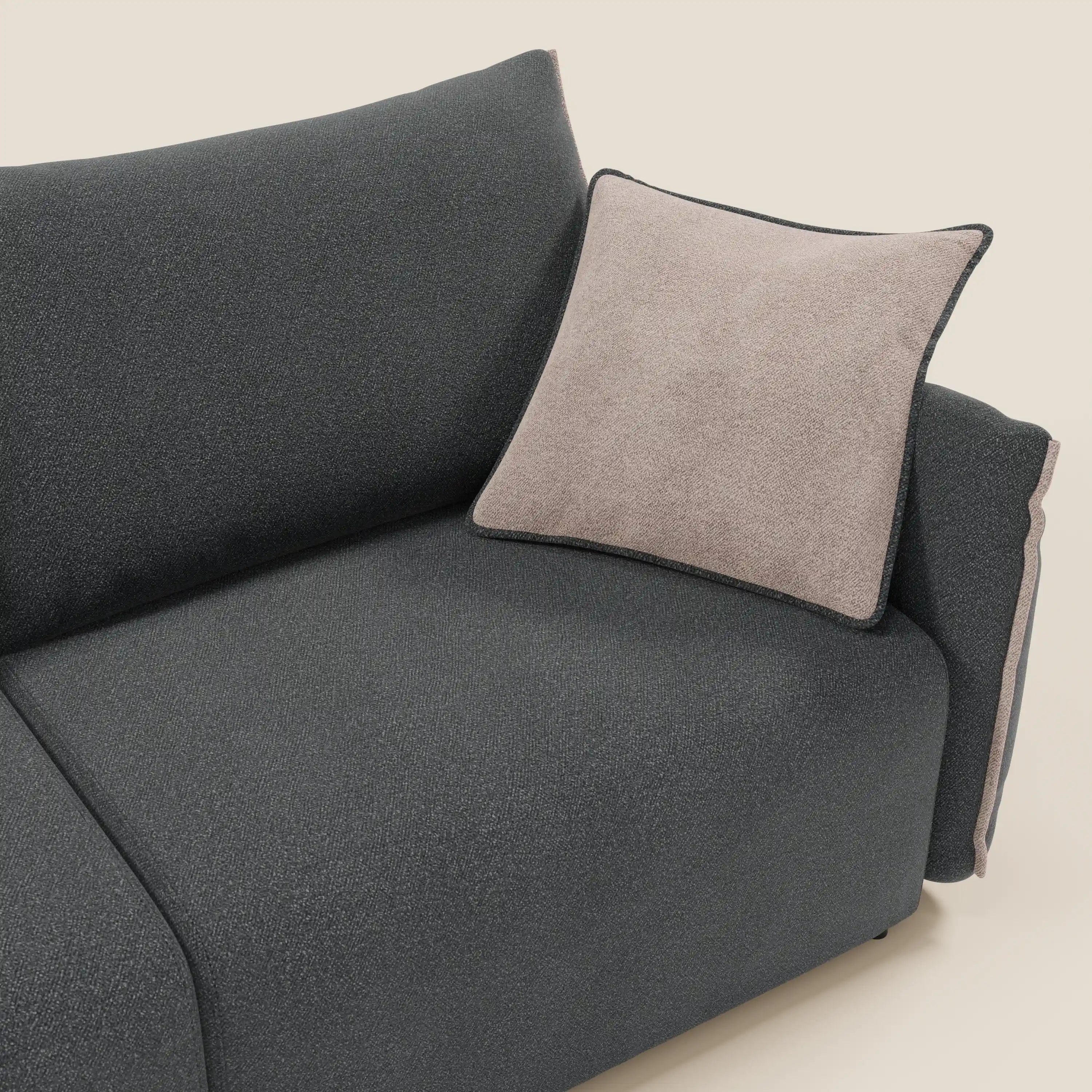 Primo piano del divano Divani.Store Flexar con sedute allungabili e schienale in piuma, in morbido bouclé impermeabile T07 antracite-rosa, con cuscino beige chiaro e profili scuri, su uno sfondo crema chiaro che ne sottolinea il look minimalista.