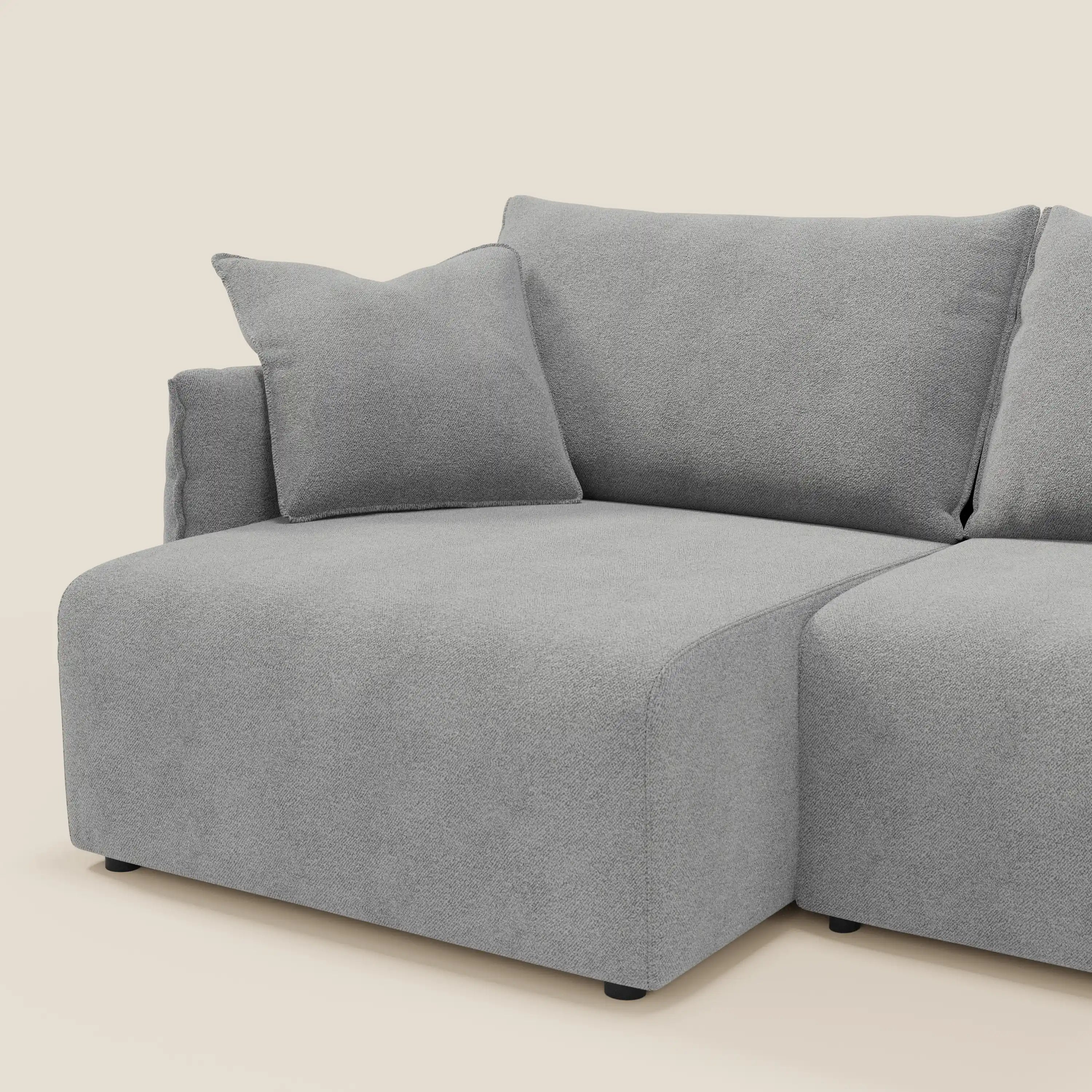 Il divano Flexar di Divani.Store è caratterizzato da sedute allungabili e da uno schienale in piuma in morbido bouclé impermeabile grigio T07. L'ampia seduta sinistra con cuscino coordinato poggia su corte gambe nere su uno sfondo beige.