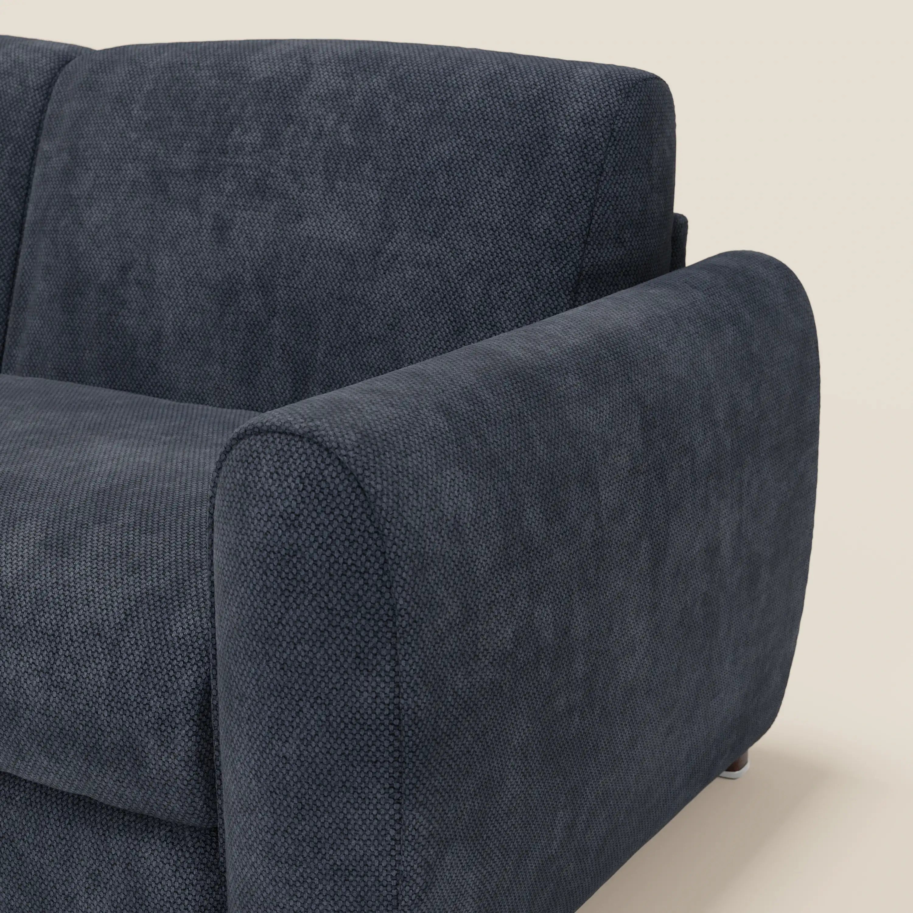 Primo piano del divano letto moderno Kaleo di Divani.Store, rivestito in raffinato tessuto impermeabile T26 blu navy, con braccioli e schienale spessi e arrotondati, su uno sfondo beige chiaro che ne evidenzia la morbida consistenza.