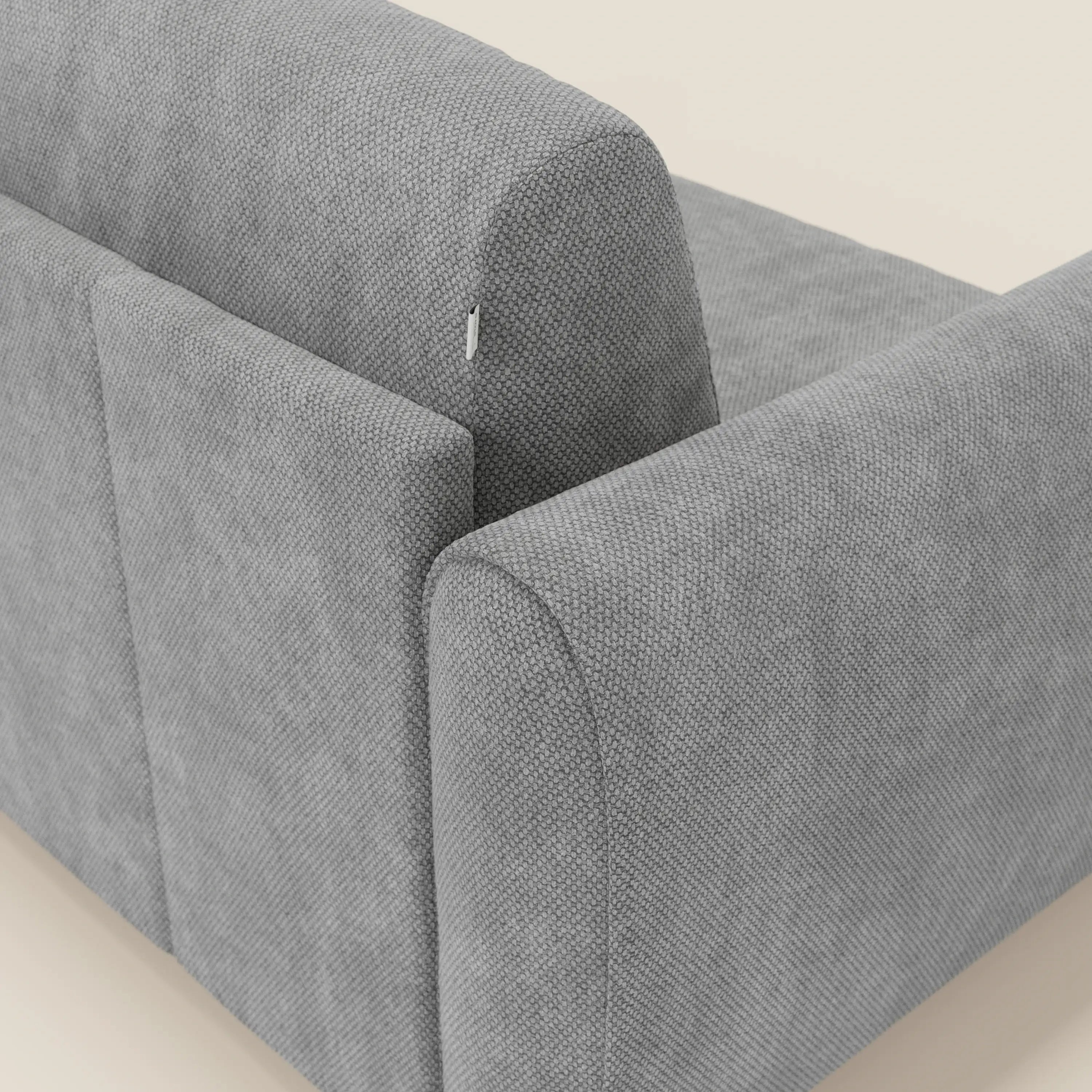 Un primo piano di Kaleo Divano letto moderno di Divani.Store ne mostra le linee pulite, il bracciolo leggermente arrotondato e la targhetta in tessuto impermeabile T26 grigio, che ne evidenzia il design contemporaneo su uno sfondo chiaro.