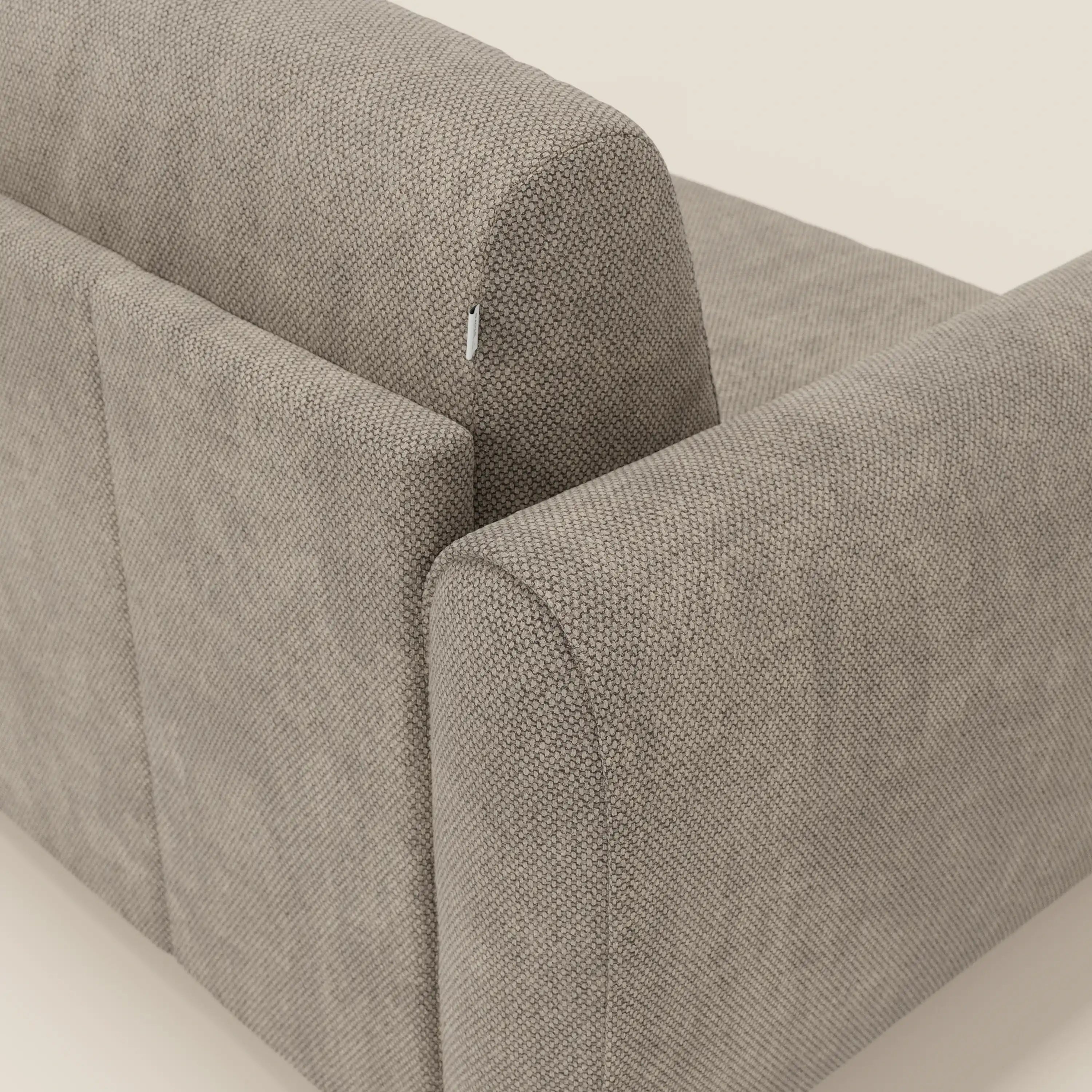 Un primo piano del divano letto moderno Kaleo con materasso H17 cm di Divani.Store in tessuto impermeabile T26 tortora, che evidenzia il suo design contemporaneo con bordi arrotondati e una piccola etichetta in tessuto sul cuscino posteriore.