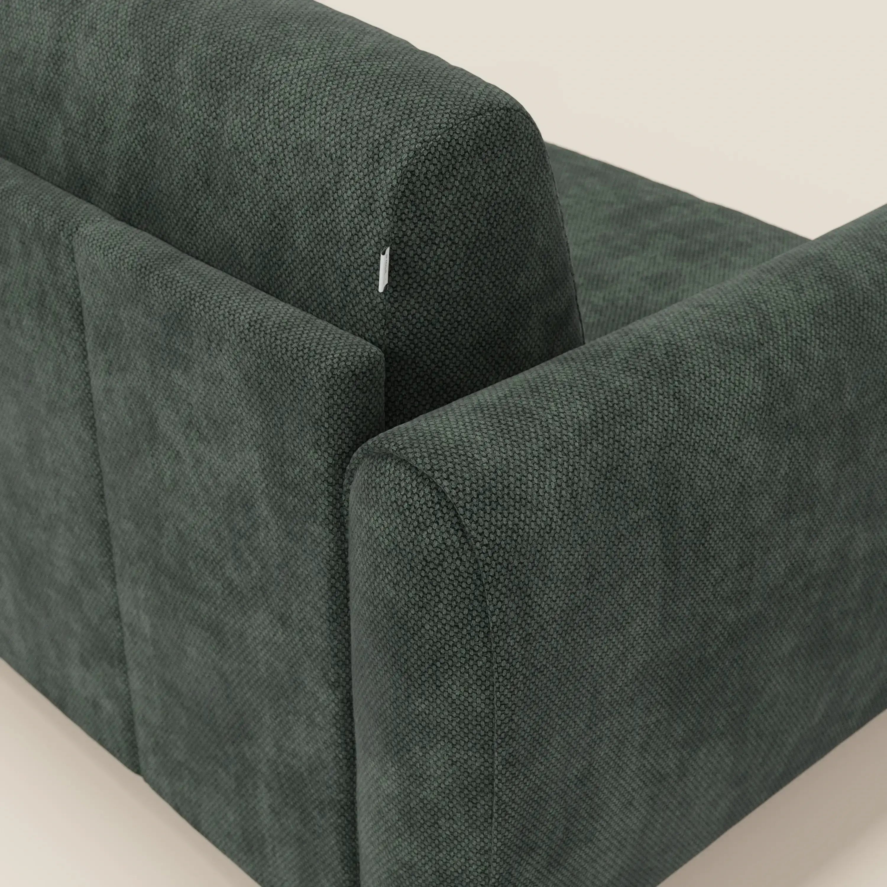 Primo piano di Kaleo Divano letto moderno di Divani.Store in tessuto impermeabile verde scuro T26, caratterizzato da ampi braccioli, schienale alto e etichetta in tessuto bianco nell'angolo superiore.