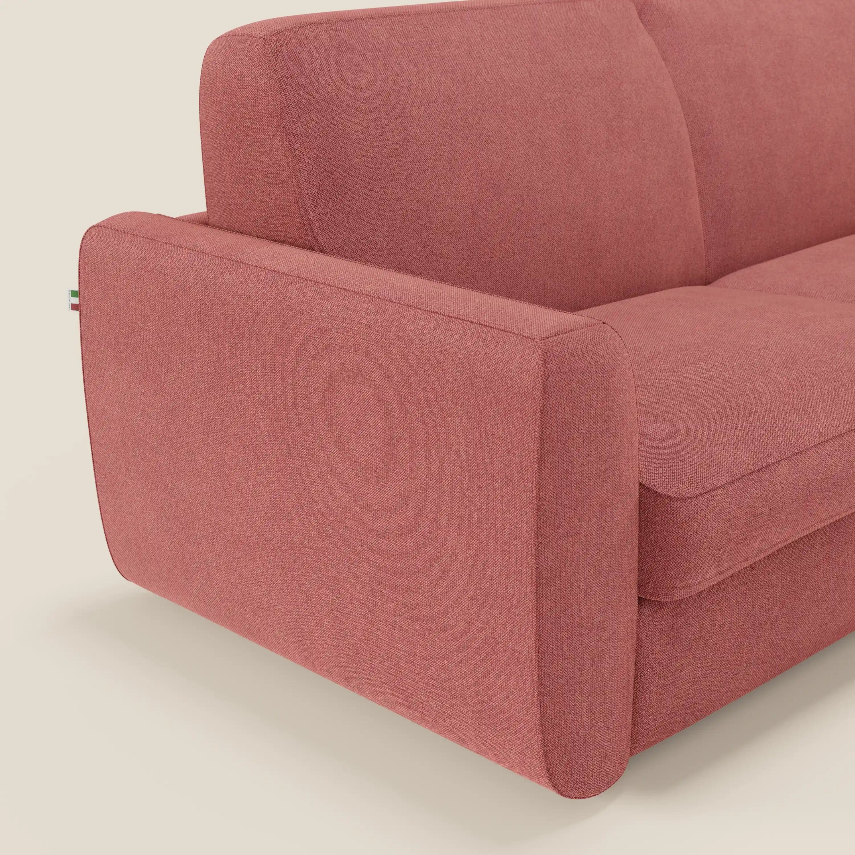 Un primo piano del divano letto sfoderabile Leonida di Divani.Store in tessuto Smacchiabile T23 rosso ciliegia mostra il bracciolo sinistro, i cuscini di seduta e la targhetta italiana, evidenziando il materasso H18 cm e il vano portaguanciali. Sfondo beige neutro.