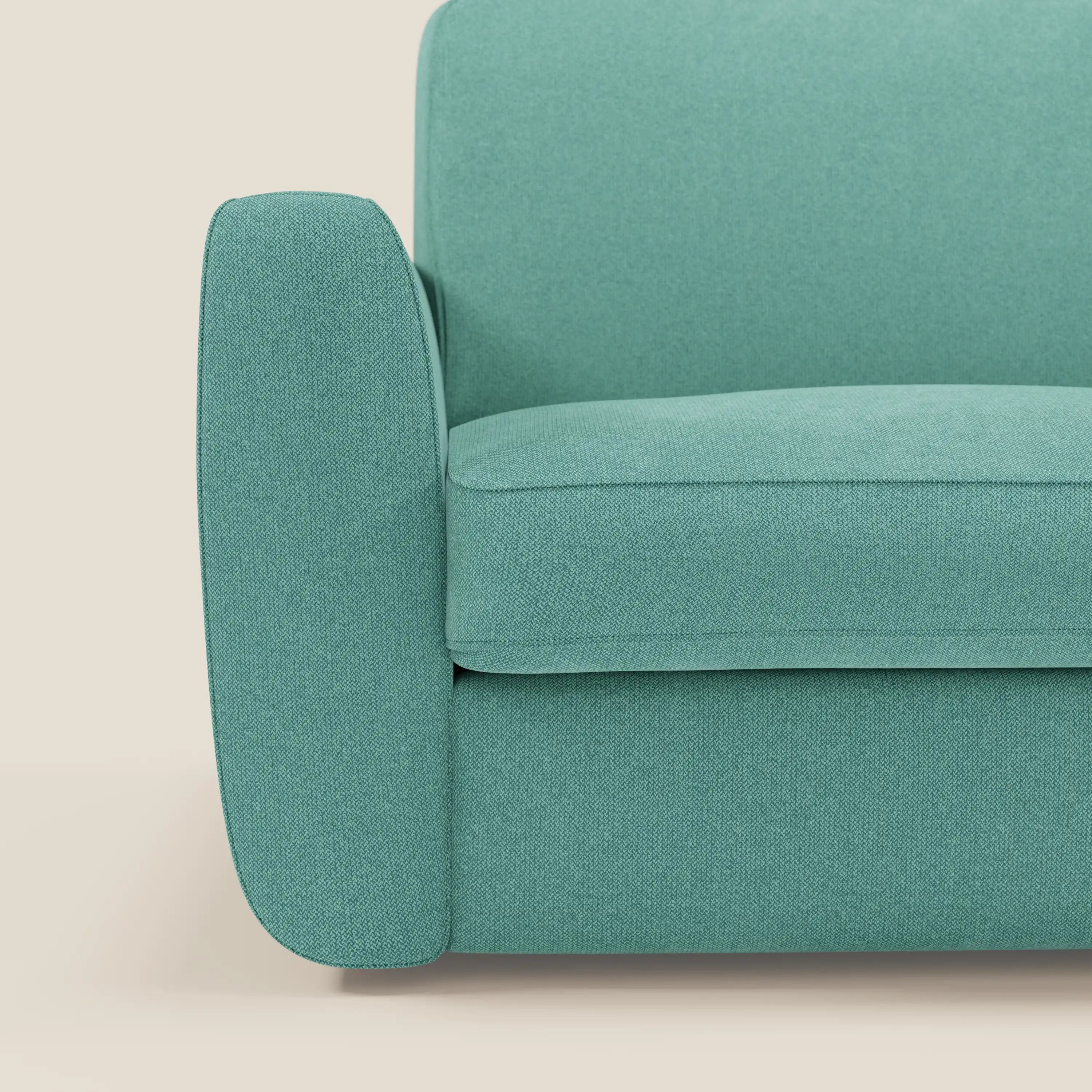 Un primo piano del divano letto sfoderabile Leonida di Divani.Store in smacchiabile T23 verde acqua mostra i bordi lisci e arrotondati del bracciolo sinistro, della seduta e dello schienale su uno sfondo beige chiaro; include un materasso H18 cm e un cuscino contenitore.