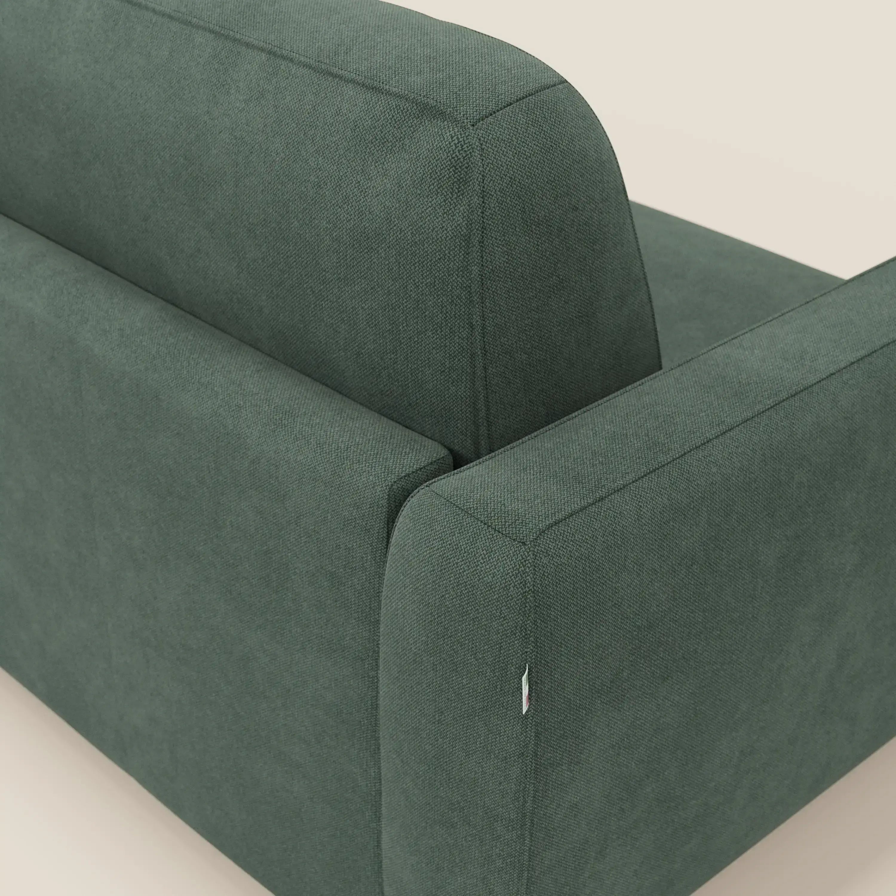 Primo piano dello schienale e del bracciolo del divano letto sfoderabile Leonida di Divani.Store, in tessuto smacchiabile T23 verde, dalle linee pulite e dalla texture morbida, su uno sfondo beige chiaro.
