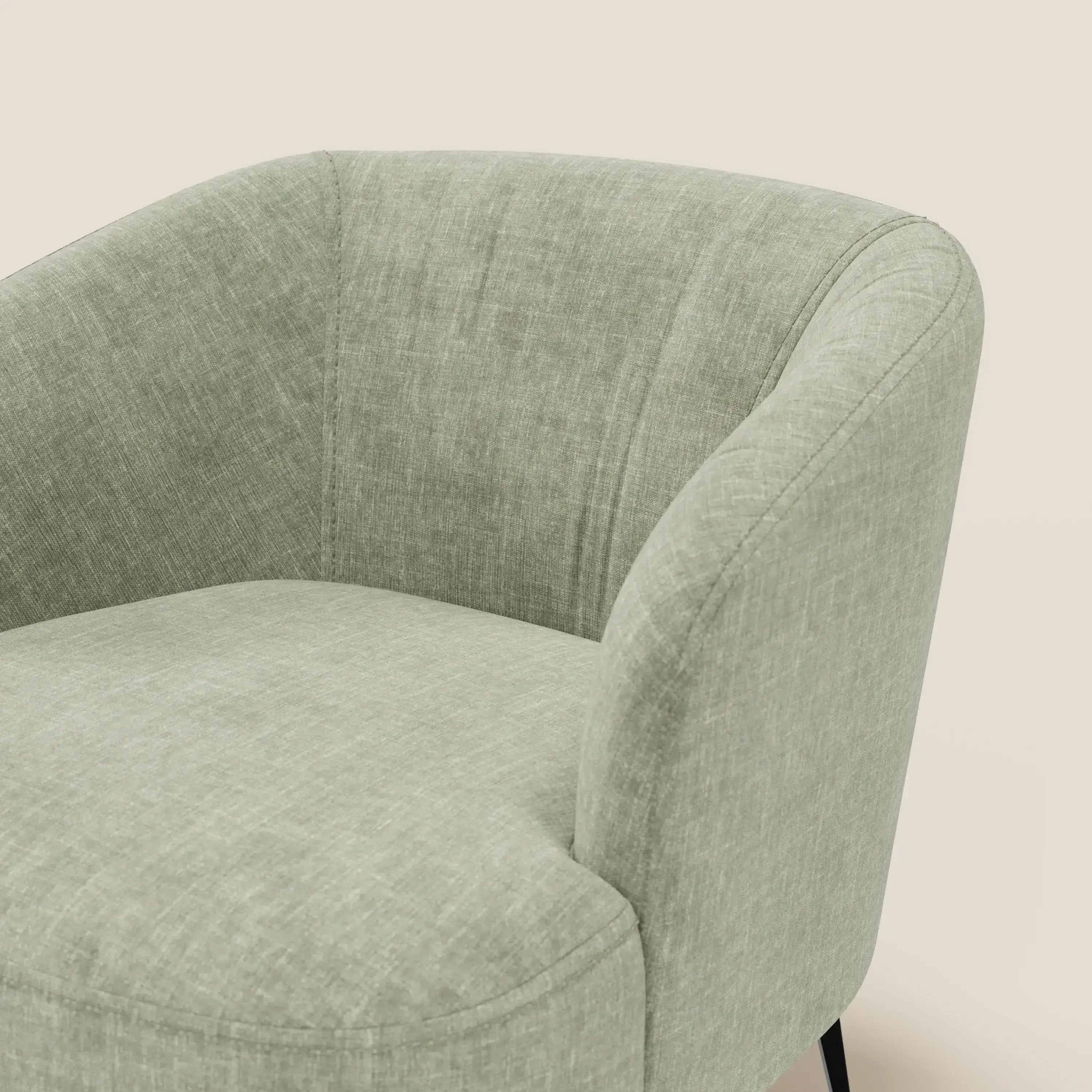 Primo piano di Renoa Poltroncina dall'eleganza moderna in tessuto smacchiabile T24 verde salvia di Divani.Store, che mostra le sottili gambe nere e il comfort morbido e avvolgente su uno sfondo bianco sporco. È visibile solo una parte della sedia.