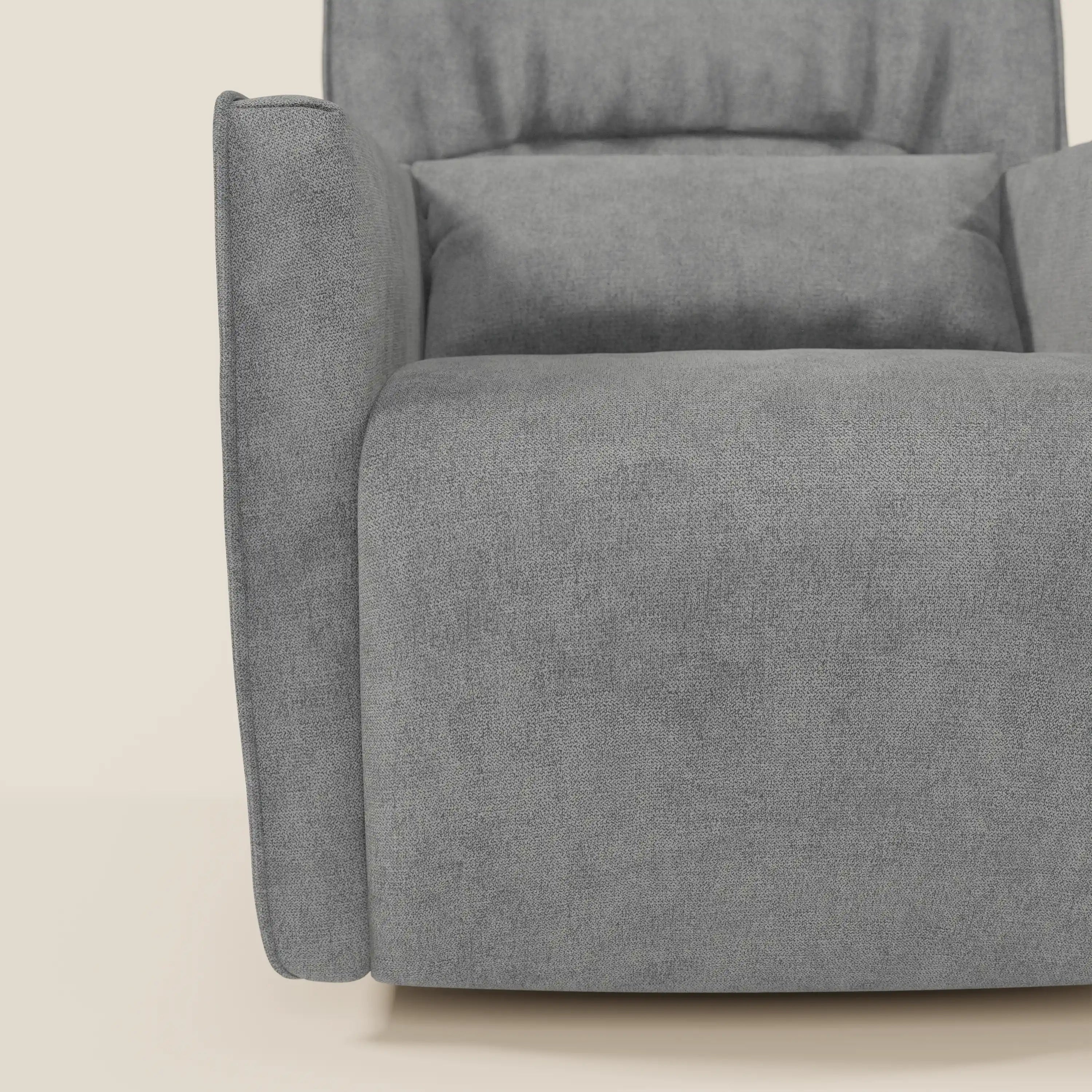Un primo piano della poltrona girevole Divani.Store Tulla in tessuto impermeabile T02 grigio mostra il bracciolo sinistro, il cuscino di seduta e lo schienale con cuscino abbinato. Il rivestimento morbido e strutturato spicca su uno sfondo bianco sporco.