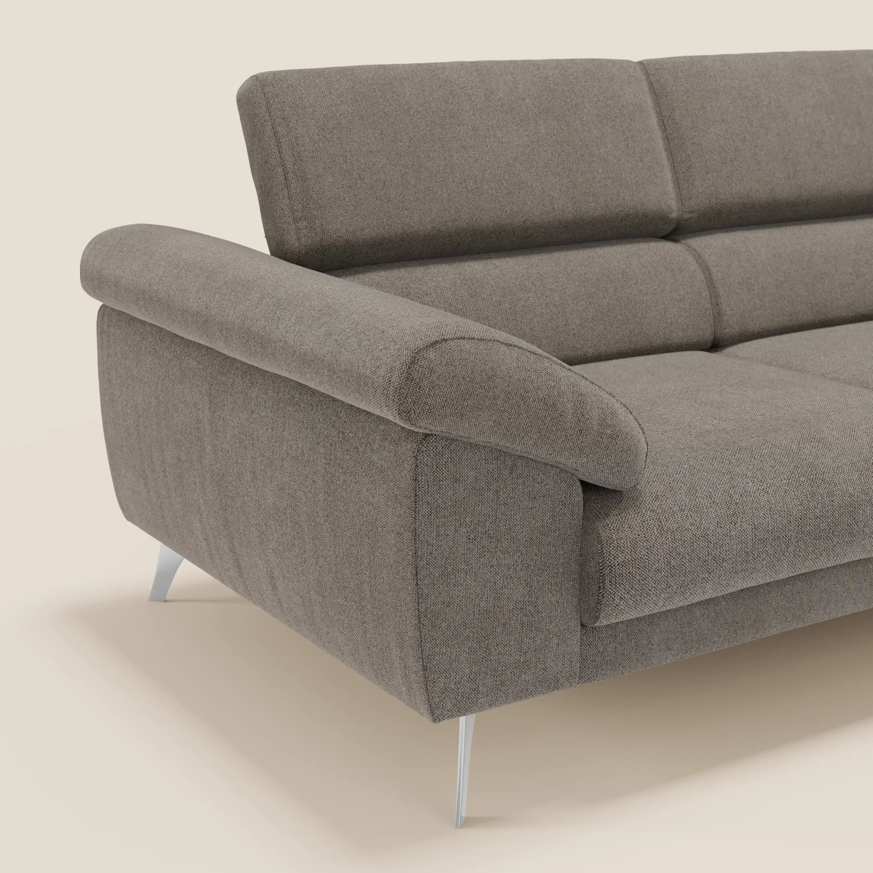 Primo piano del divano Donatello con sedute allungabili di Divani.Store, rivestito in tessuto smacchiabile T23 talpa, con braccioli contenitore, poggiatesta reclinabili e gambe in metallo su sfondo beige.