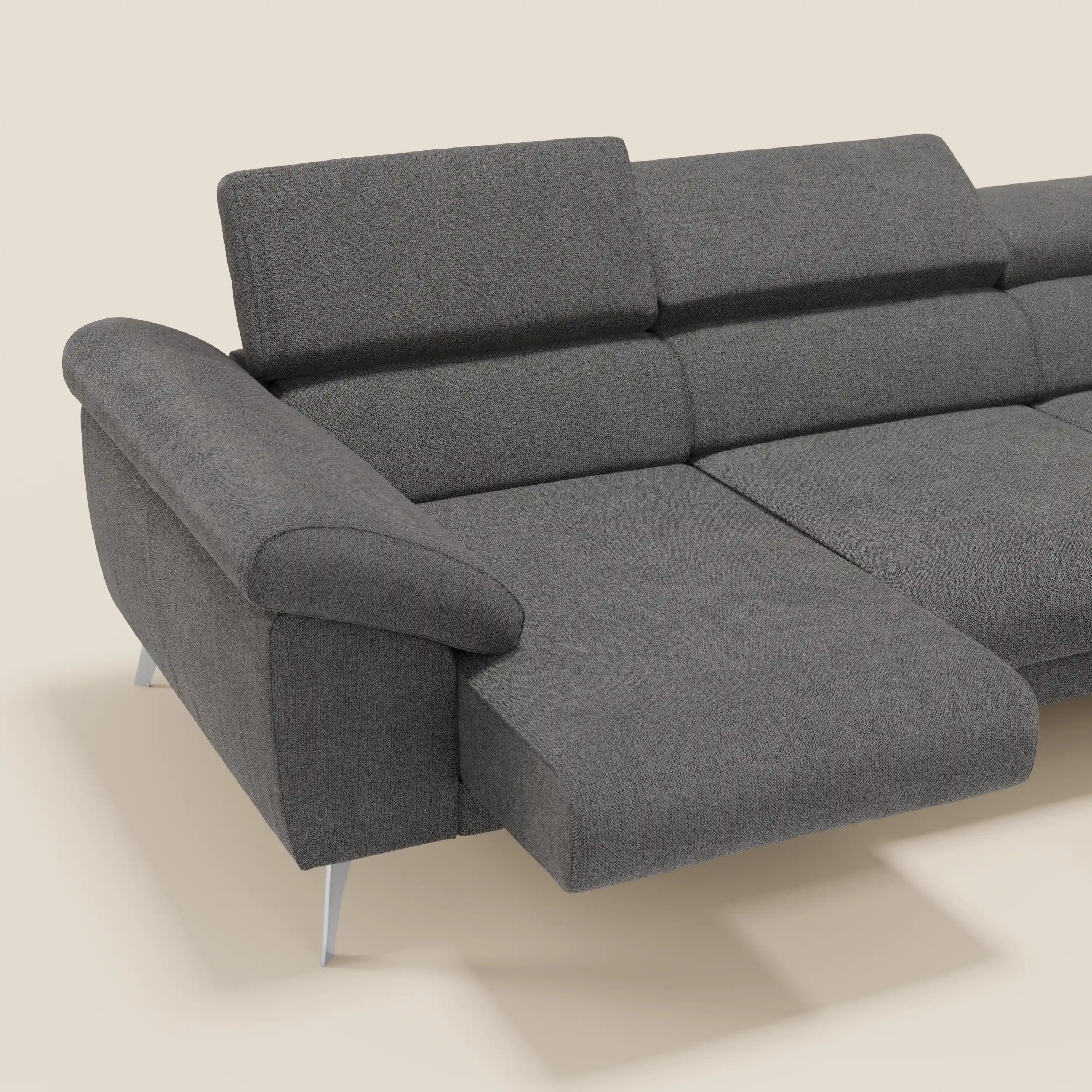 Il divano angolare Donatello di Divani.Store in morbido tessuto antracite T23 antimacchia è caratterizzato da sedute scorrevoli, braccioli contenitore, poggiatesta regolabile e una versatile penisola reversibile su uno sfondo beige chiaro.
