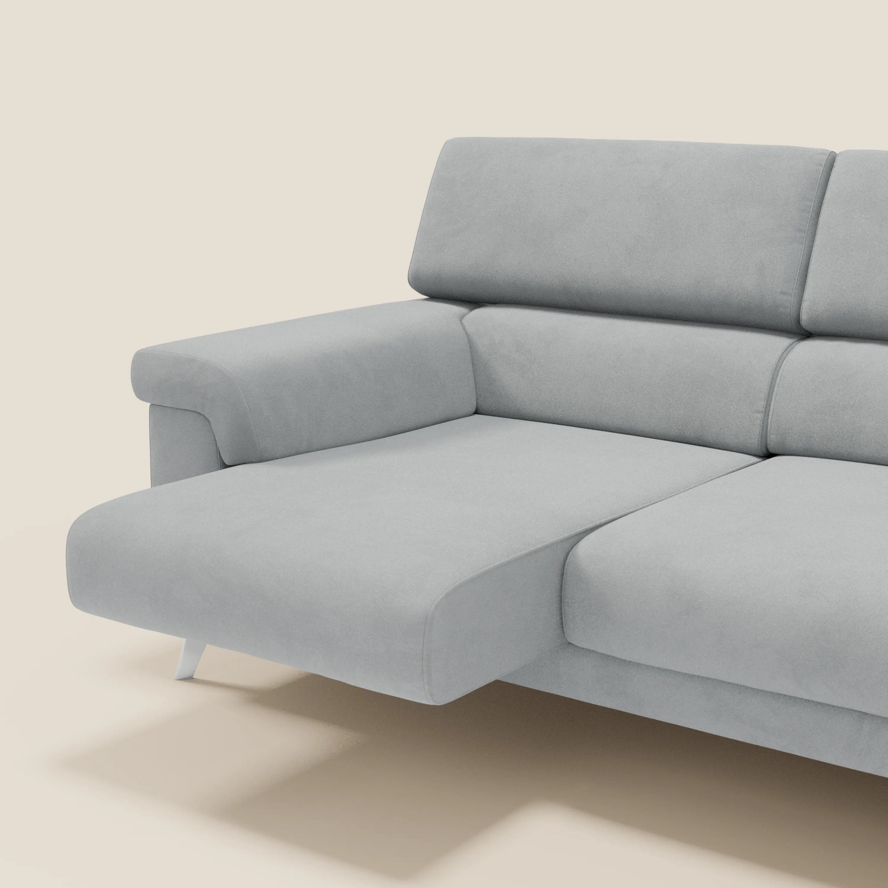 Divano angolare Raffaello contemporaneo di Divani.Store in microfibra antimacchia T11 grigio chiaro, con sedute scorrevoli e poggiatesta regolabili. Solo una parte del divano è visibile sullo sfondo beige.